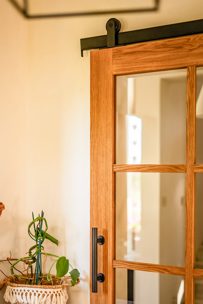 Teilansicht einer Eichen-Schiebetür mit schwarzem, vertikalem Metallgriff und einer durch Sprossen unterteilten Glasscheibe.