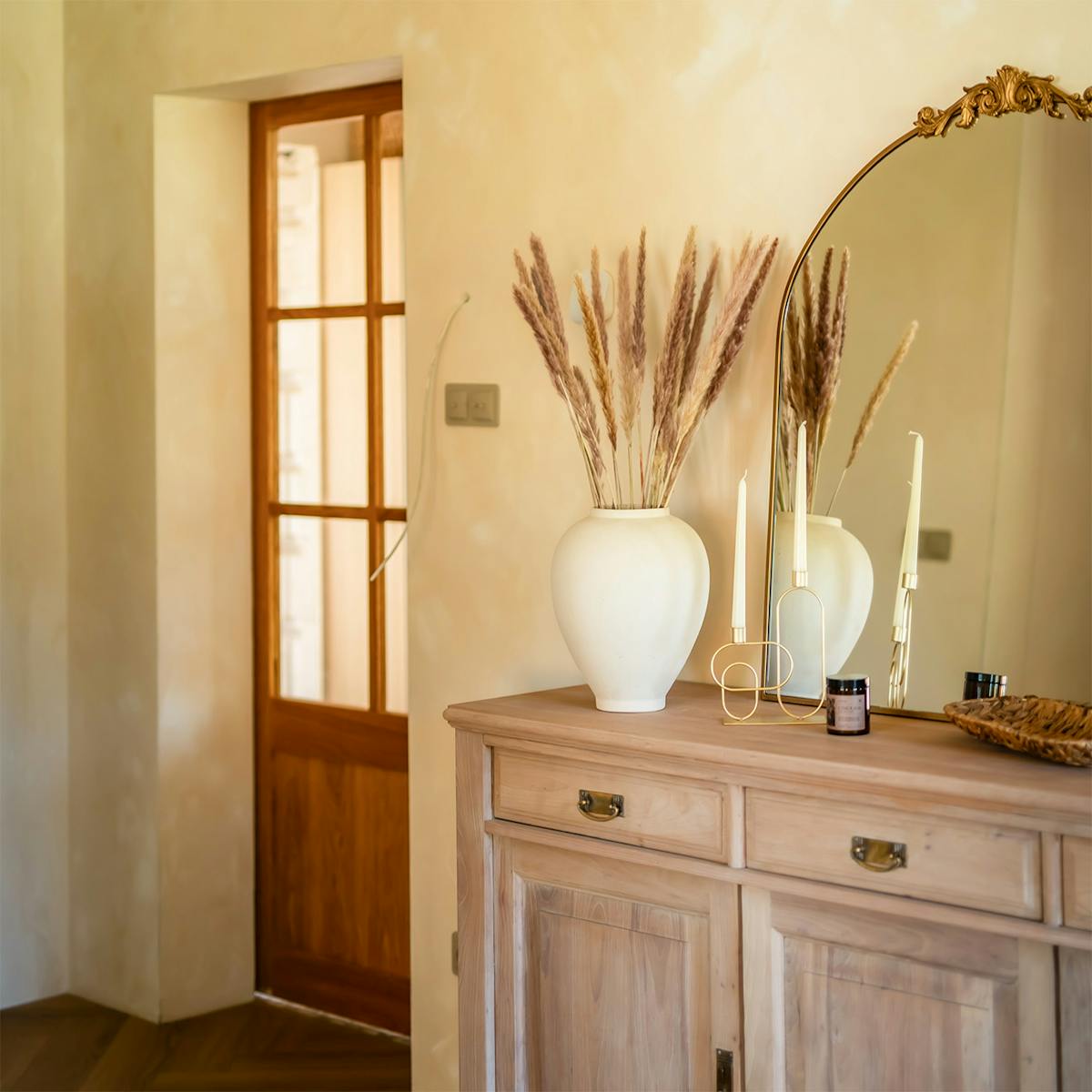 Holzkonsolen mit Spiegel und Vase im Flur, im Hintergrund rustikale Eichenholztüren mit Glasfüllung.