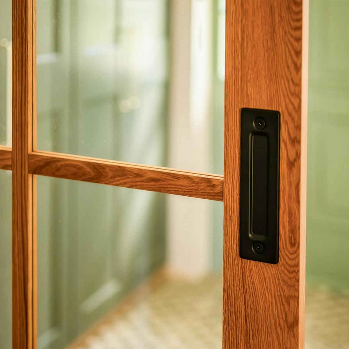 Detail einer Eichen-Schiebetür im Modern-Farmhouse-Stil: schwarzer matter Griffschalengriff, sichtbare Holzmaserung und Glaseinsätze mit Sprossen.