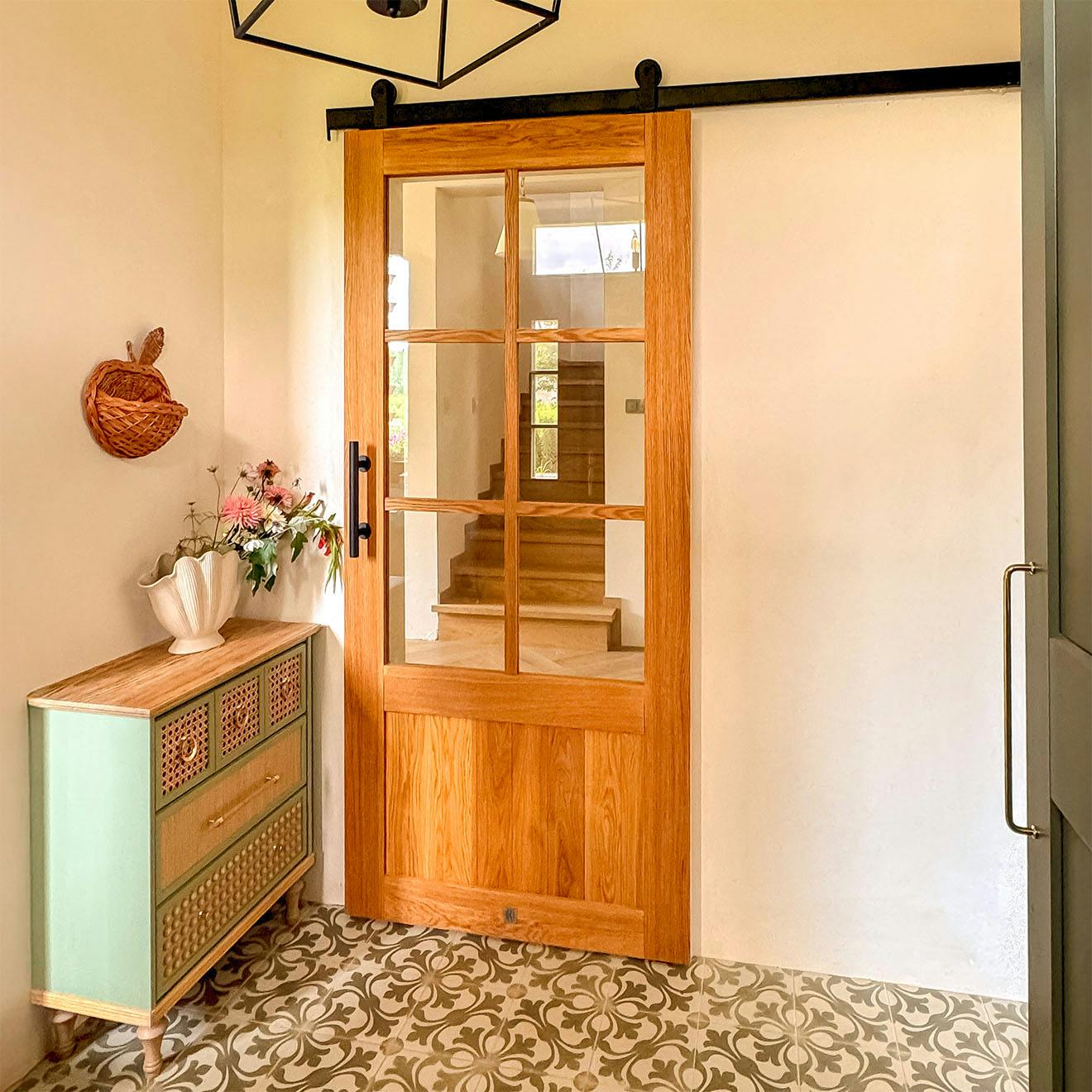 Portes coulissantes vitrées en chêne dans un vestibule aménagé avec une commode vert sauge et des carreaux de ciment à motifs.