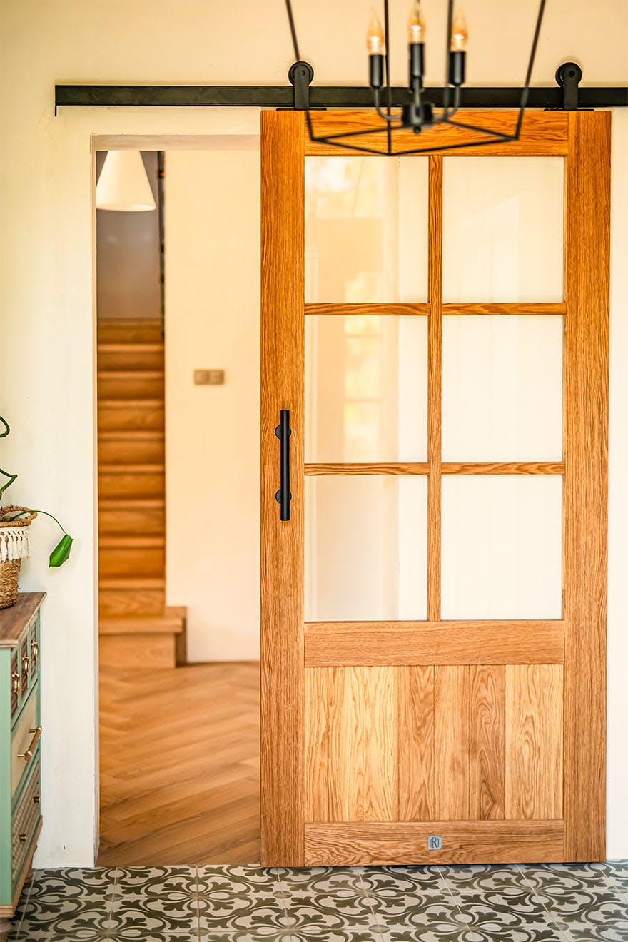 Porte coulissante en chêne de style "barn door" avec vitrage et petits bois, séparant le vestibule du couloir dans un esprit modern farmhouse.