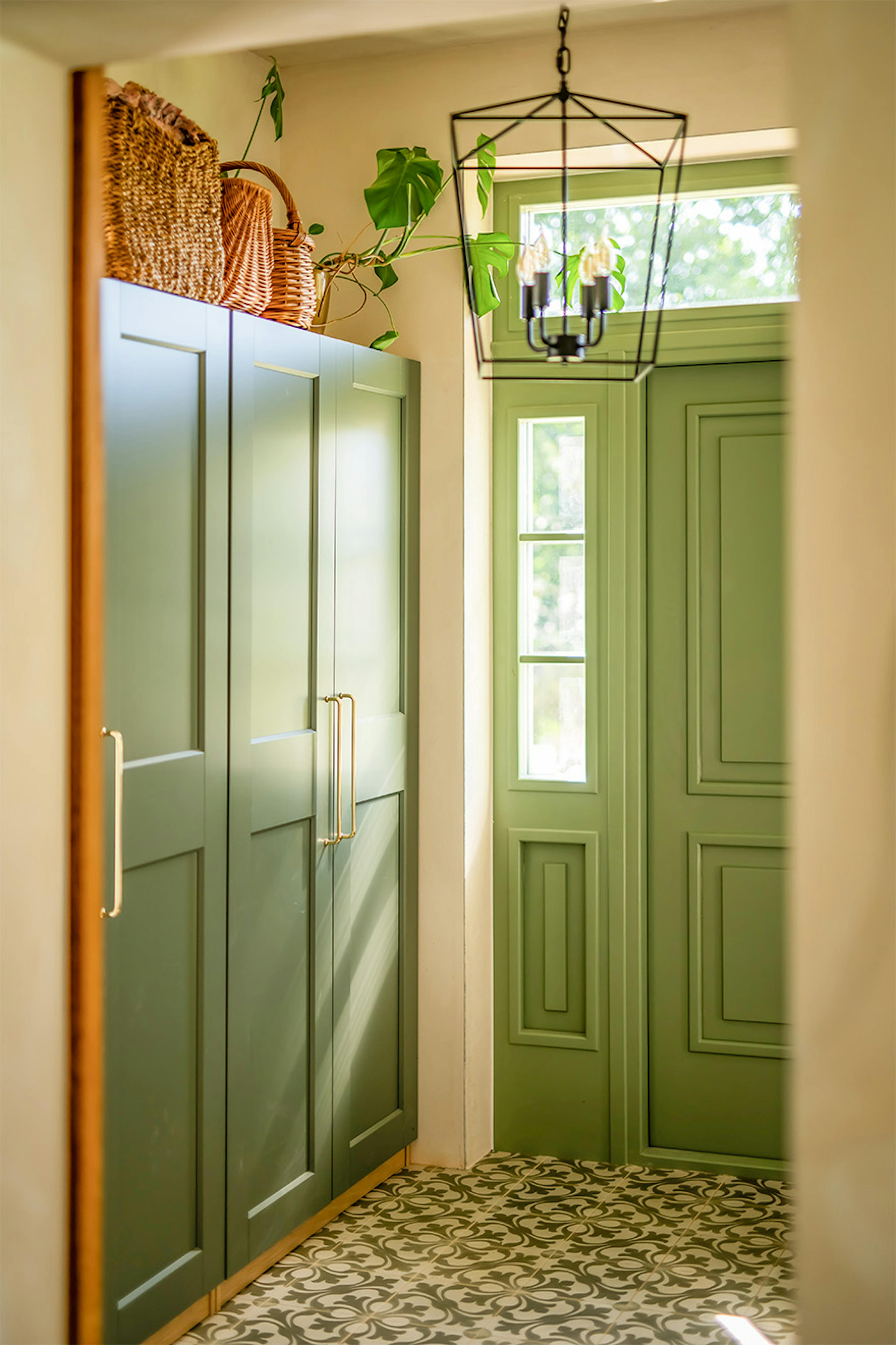 Intérieur d'un vestibule de style modern farmhouse : armoires encastrées vert sauge, porte d'entrée verte et sol à motifs.