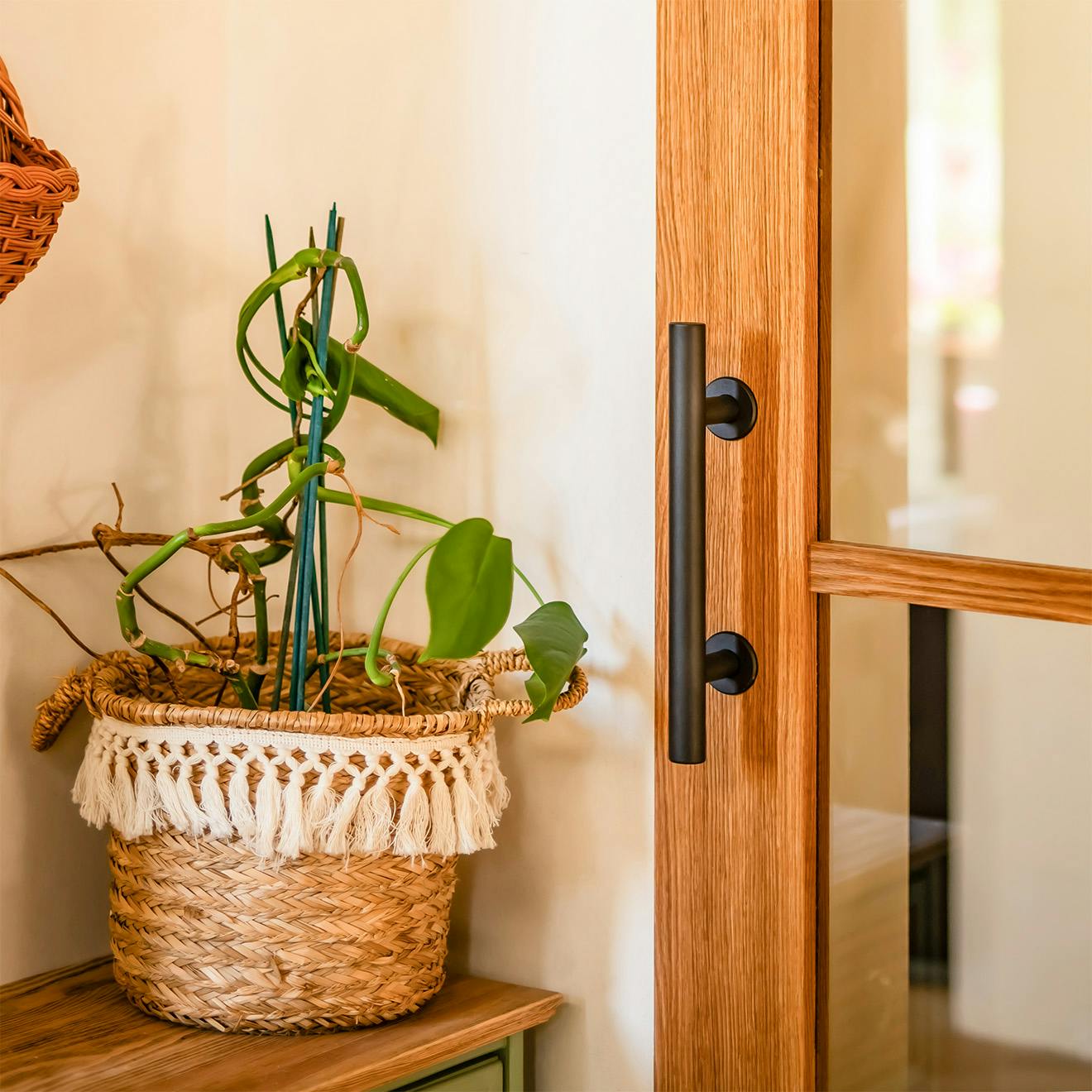 Poignée noire sur une porte coulissante en chêne, à côté d'une décoration dans un panier tressé posé sur une commode en bois.