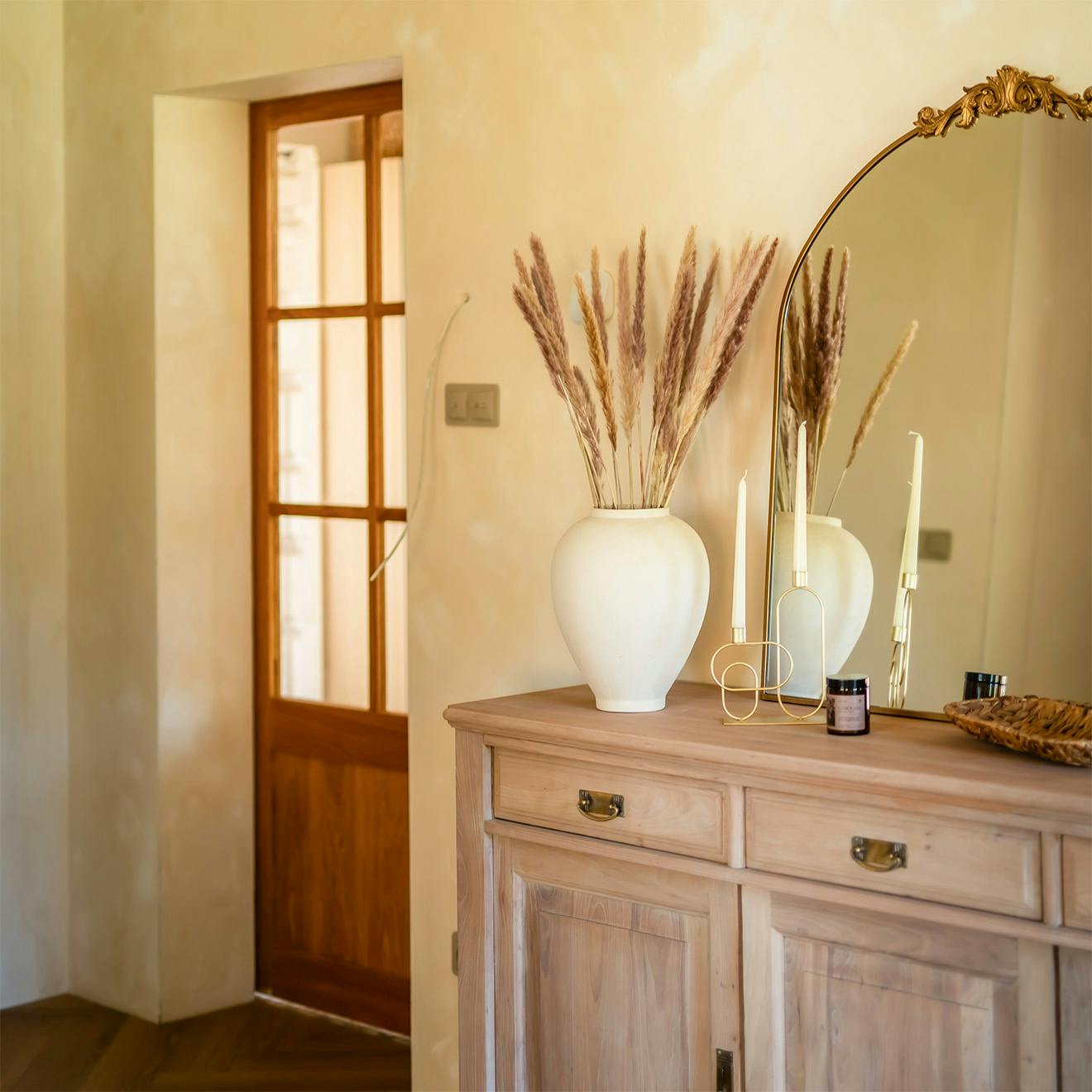 Console en bois avec miroir et vase dans une entrée, avec des portes vitrées en chêne de style rustique visibles à l'arrière-plan.