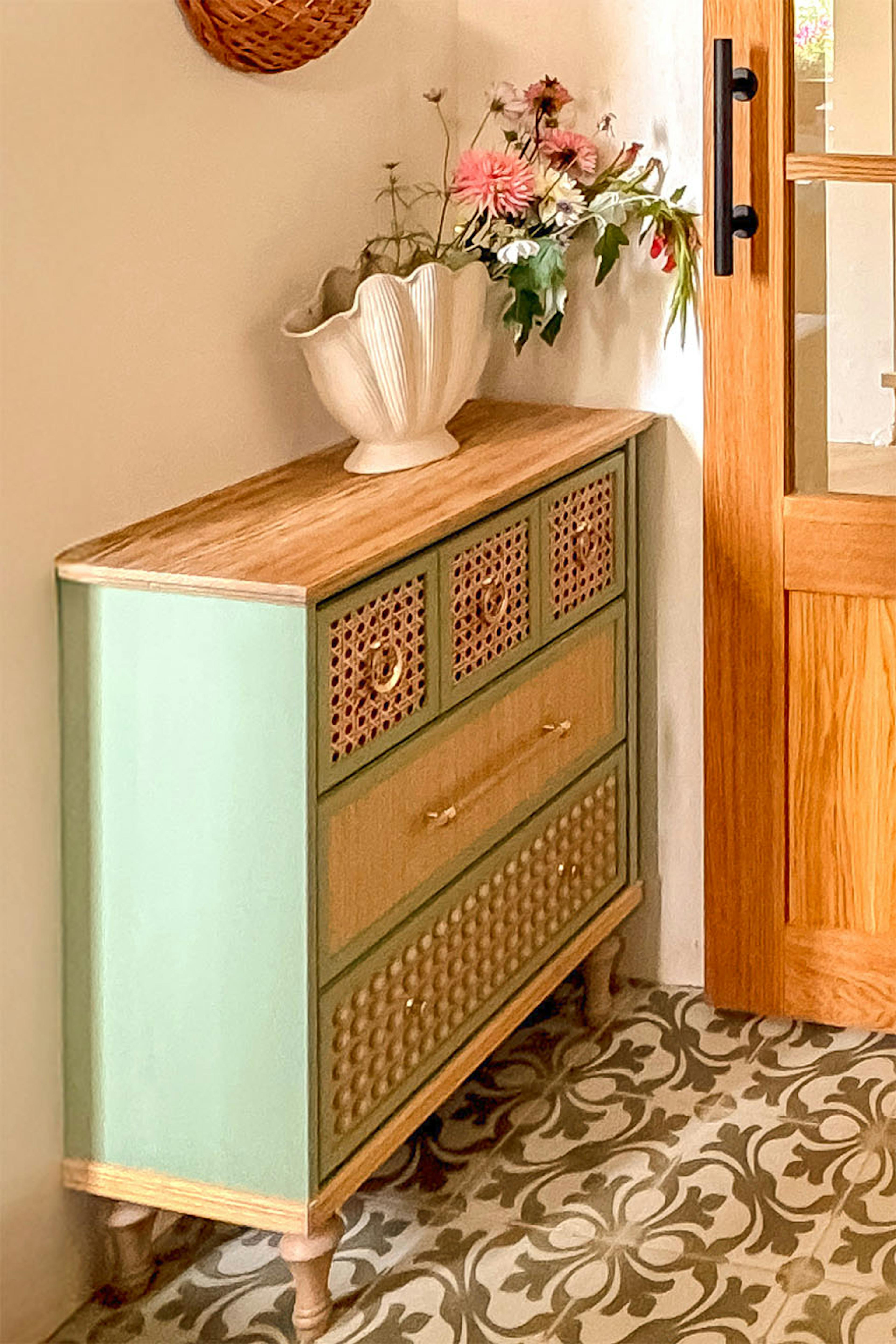 Commode vert sauge avec façades en rotin et poignées dorées installée dans un vestibule.