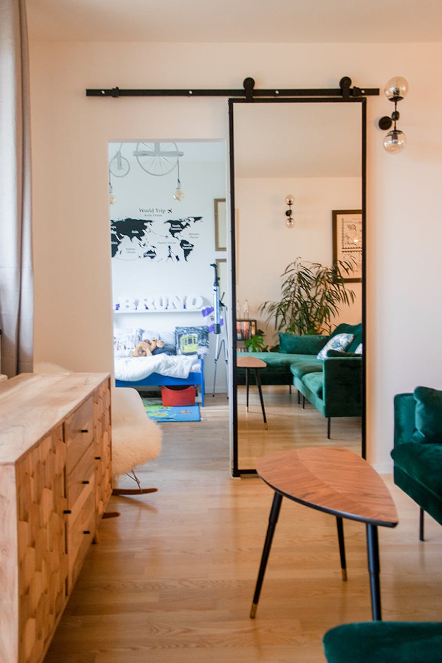 Schiebetür mit Spiegel, Tür mit Spiegel in einem Metallrahmen, Schiebetür in einem modernen Interieur, grünes Sofa, Kommode im modernen Stil, Tisch im skandinavischen Stil