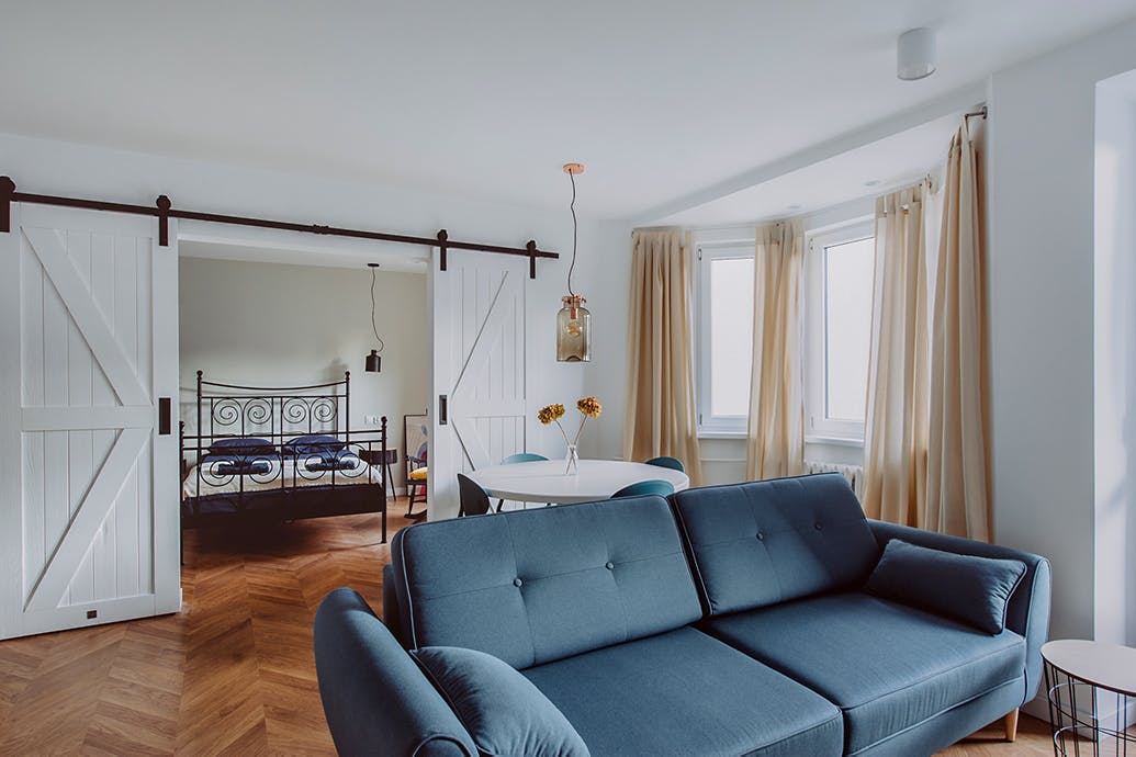 un canapé bleu dans un salon décloisonné séparé de la chambre par une porte coulissante blanche