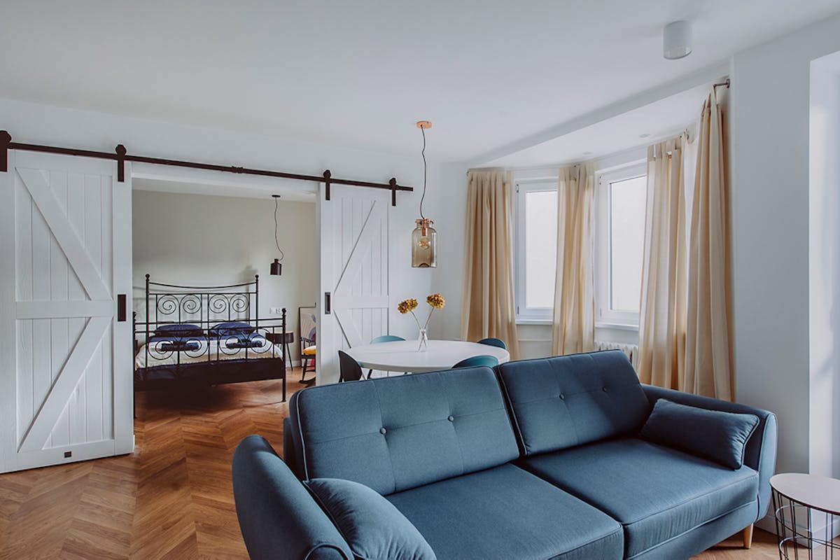 Blaues Sofa in einem offenen Wohnzimmer, das durch eine weiße Schiebetür vom Schlafzimmer getrennt ist