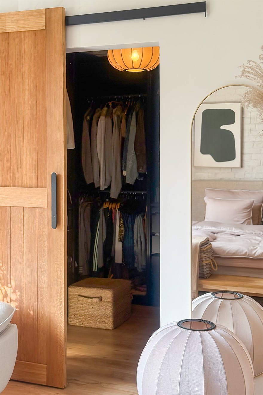 The wardrobe is accessed via an oak sliding door. Inside, the clothes are neatly arranged, with a mirror and designer floor lamps beside them.