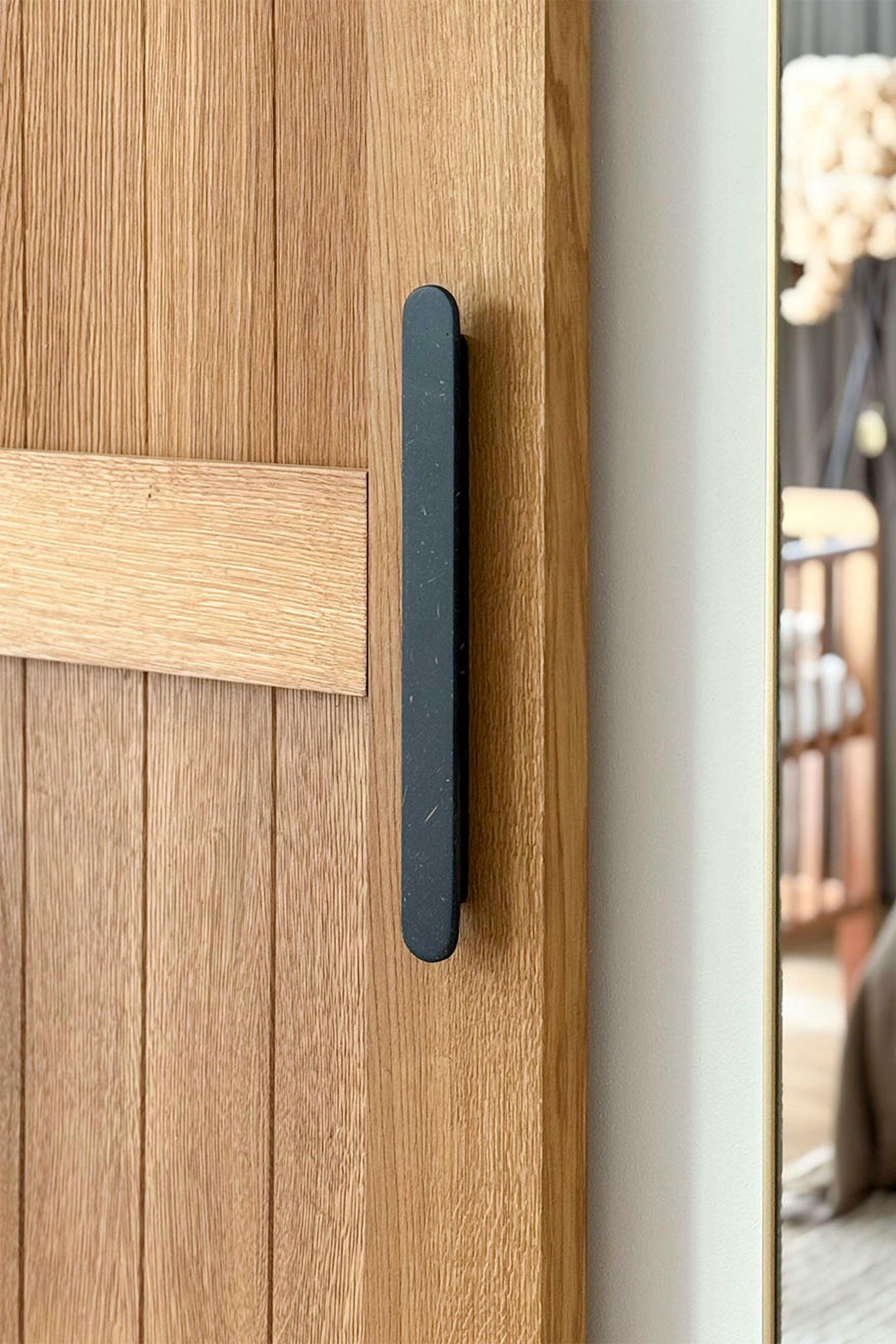 Gros plan sur la poignée noire et allongée d'une porte coulissante en chêne. Ce détail souligne le design moderne et contraste avec la texture naturelle du bois de chêne.