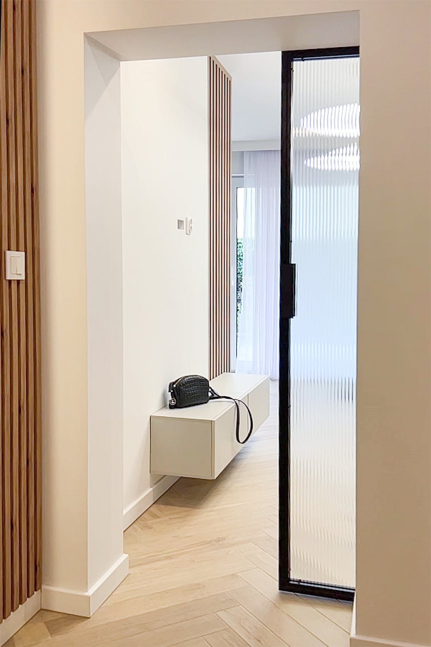 Przejście między salonem a korytarzem z wykorzystaniem drzwi przesuwnych ze szkłem typu flutes.