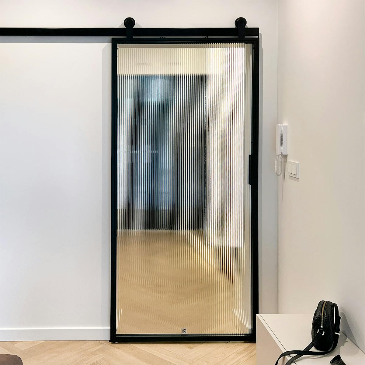 Drzwi przesuwne ze szkłem typu flutes łączące minimalistyczny salon z przedpokojem.