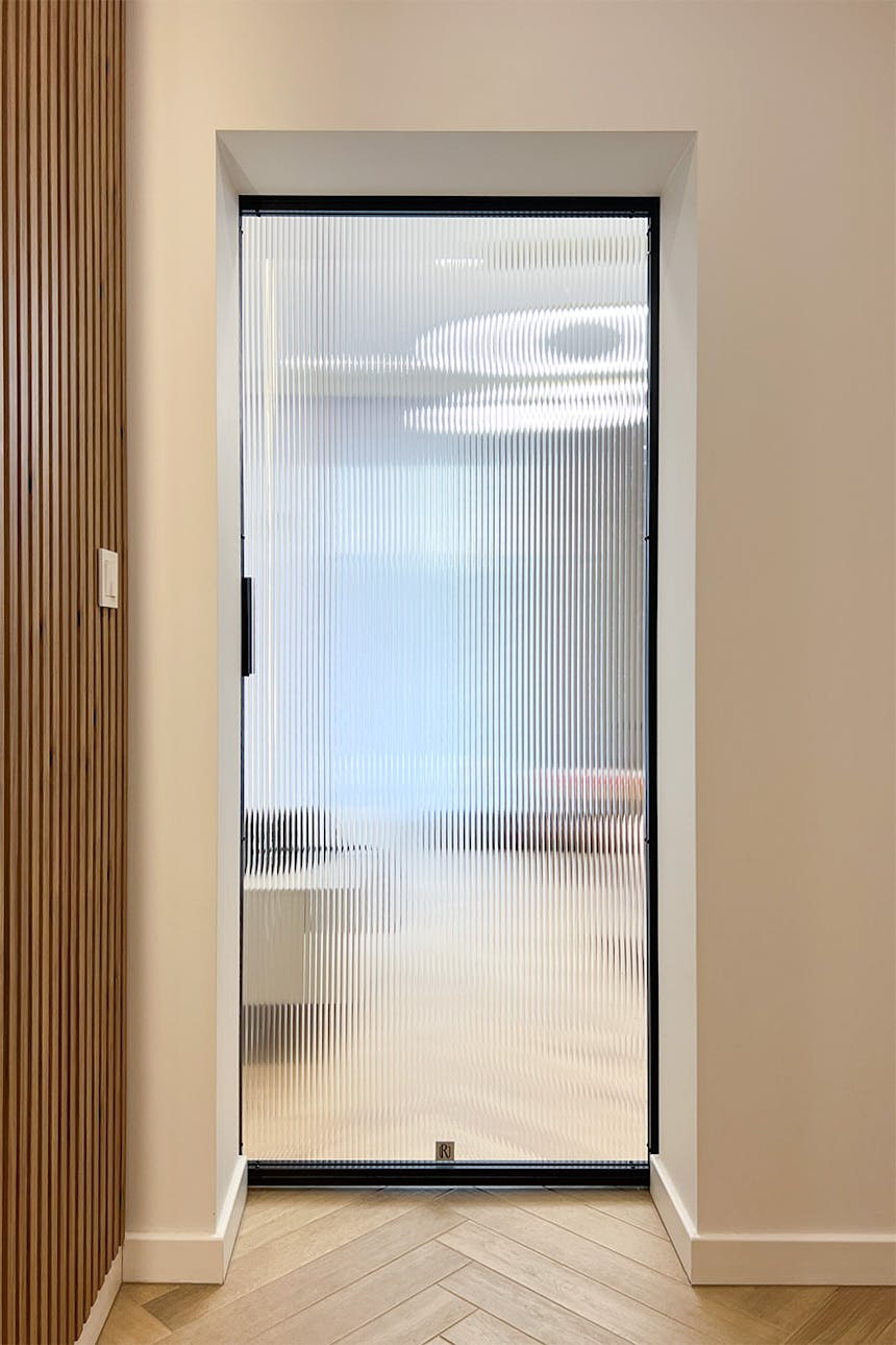 Minimalistyczny przedpokój z drzwiami przesuwnymi, widok z korytarza w stronę salonu przez ryflowaną szybę.