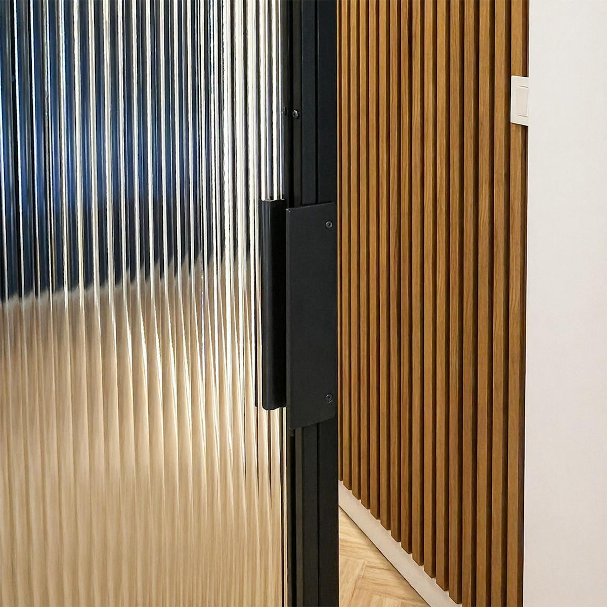 Detal czarnego pionowego uchwytu na stalowej ramie drzwi przesuwnych ze szkłem.