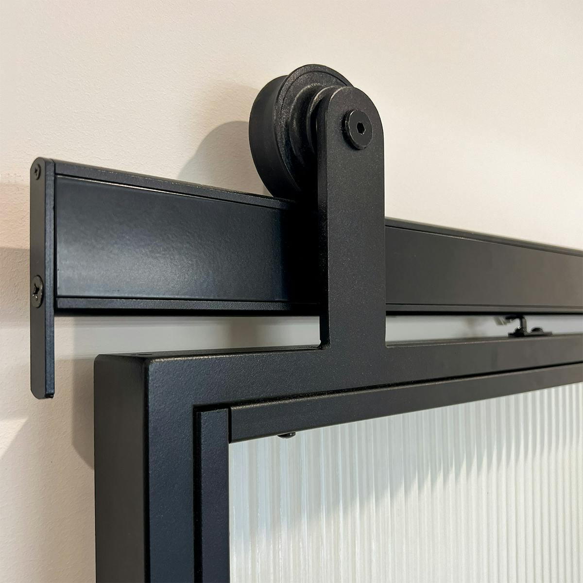 Czarny system przesuwny Reno Smart na drzwiach ze szkłem ryflowanym, zbliżenie na rolkę i prowadnicę.