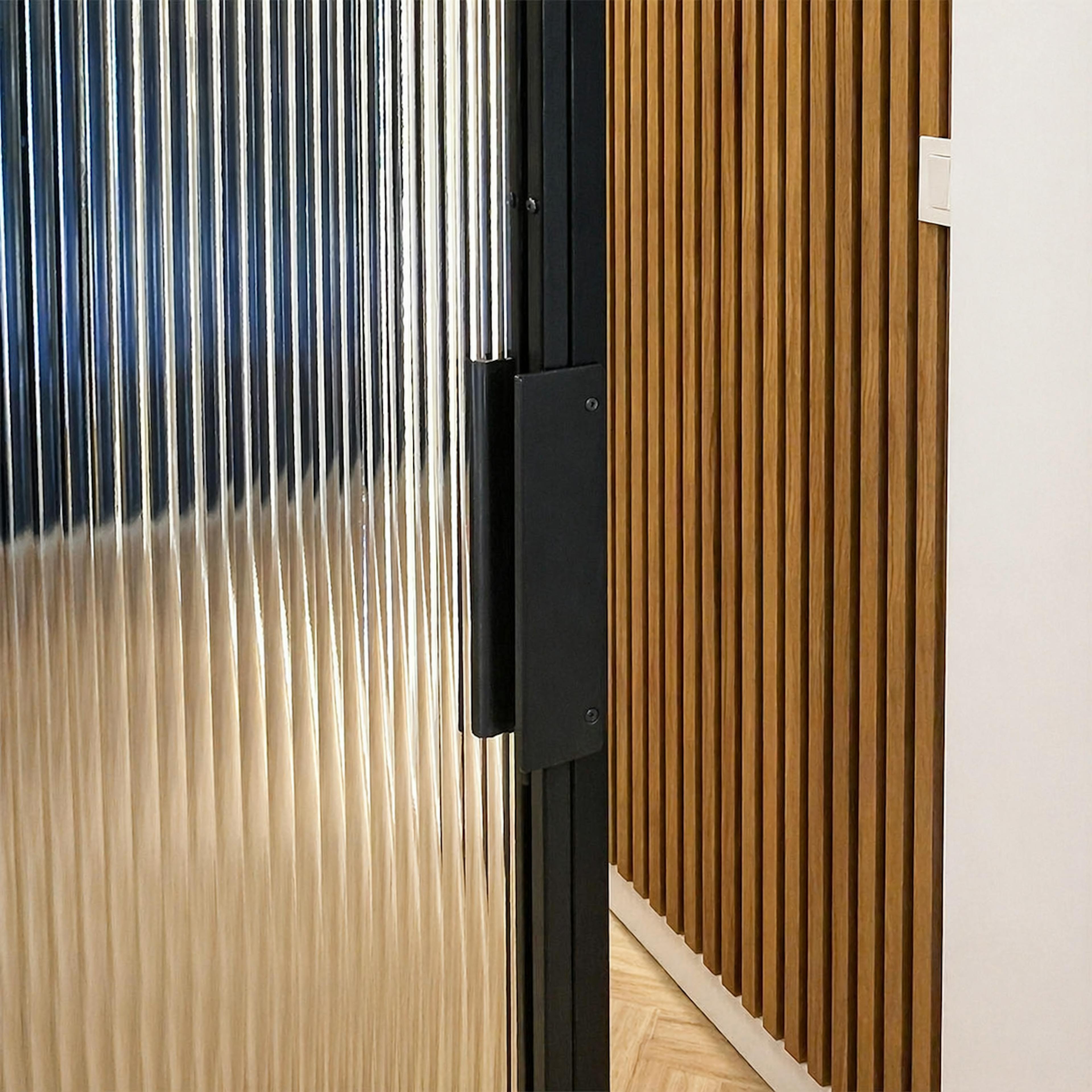Gros plan sur la poignée verticale noire fixée au cadre en acier d'une porte coulissante en verre.