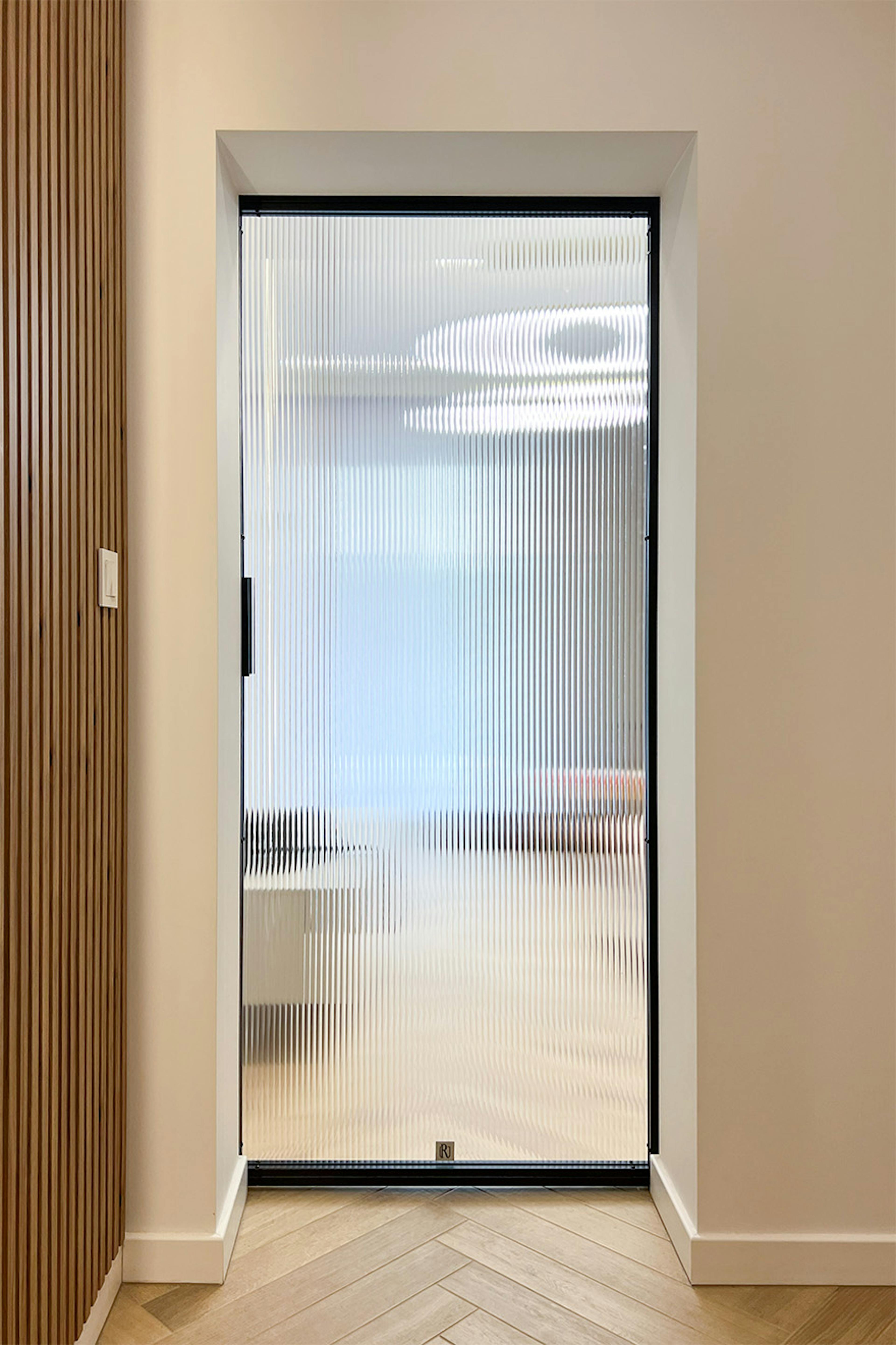 Un couloir minimaliste avec des portes coulissantes ; vue depuis le couloir vers le salon à travers une vitre cannelée.