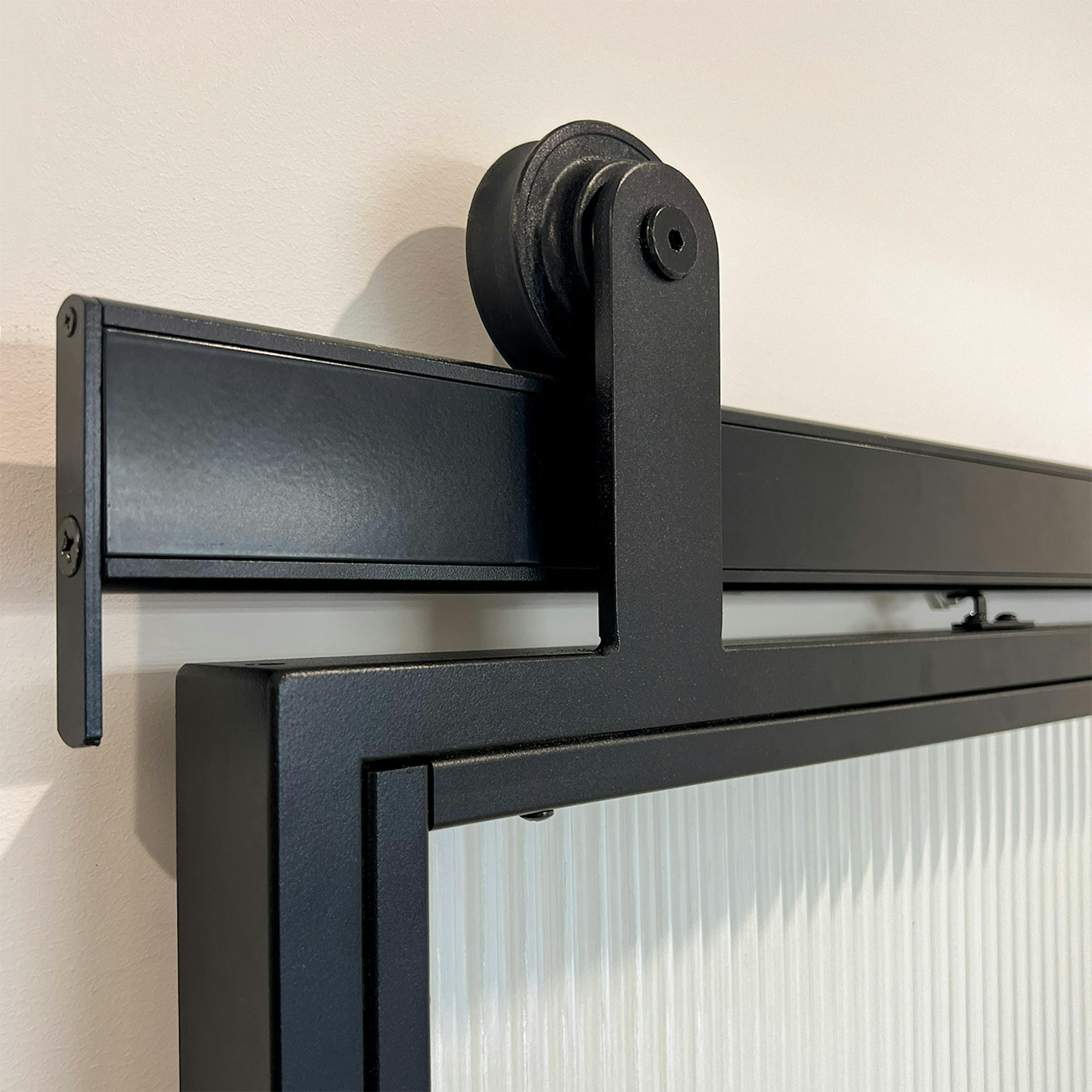 Le système coulissant Reno Smart noir sur une porte en verre cannelé, gros plan sur le rouleau et le rail de coulissement.