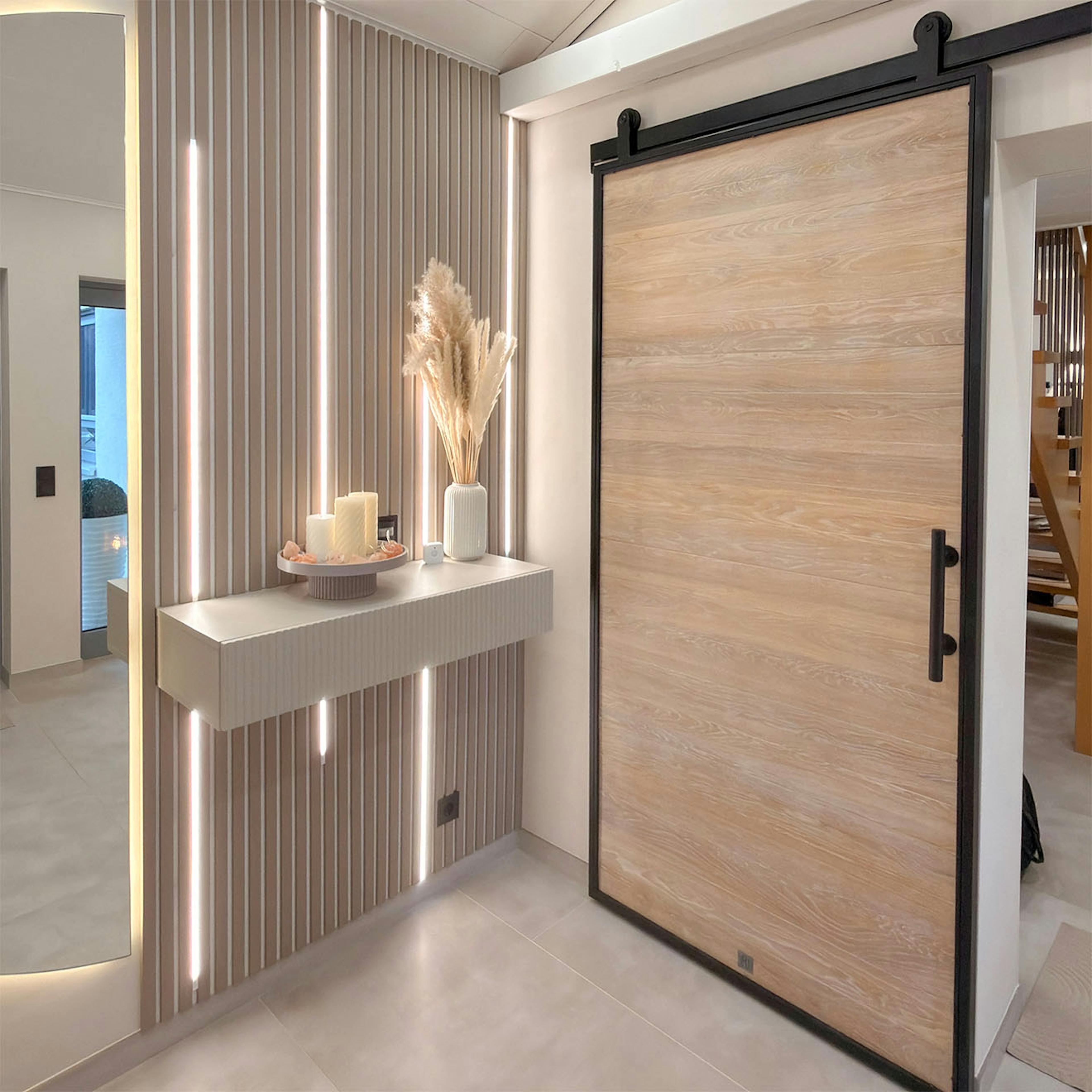 Un hall d'entrée moderne au style minimaliste et chaleureux. Au mur, des lattes décoratives avec un éclairage LED vertical et une console murale, ainsi que des portes coulissantes en chêne de style loft