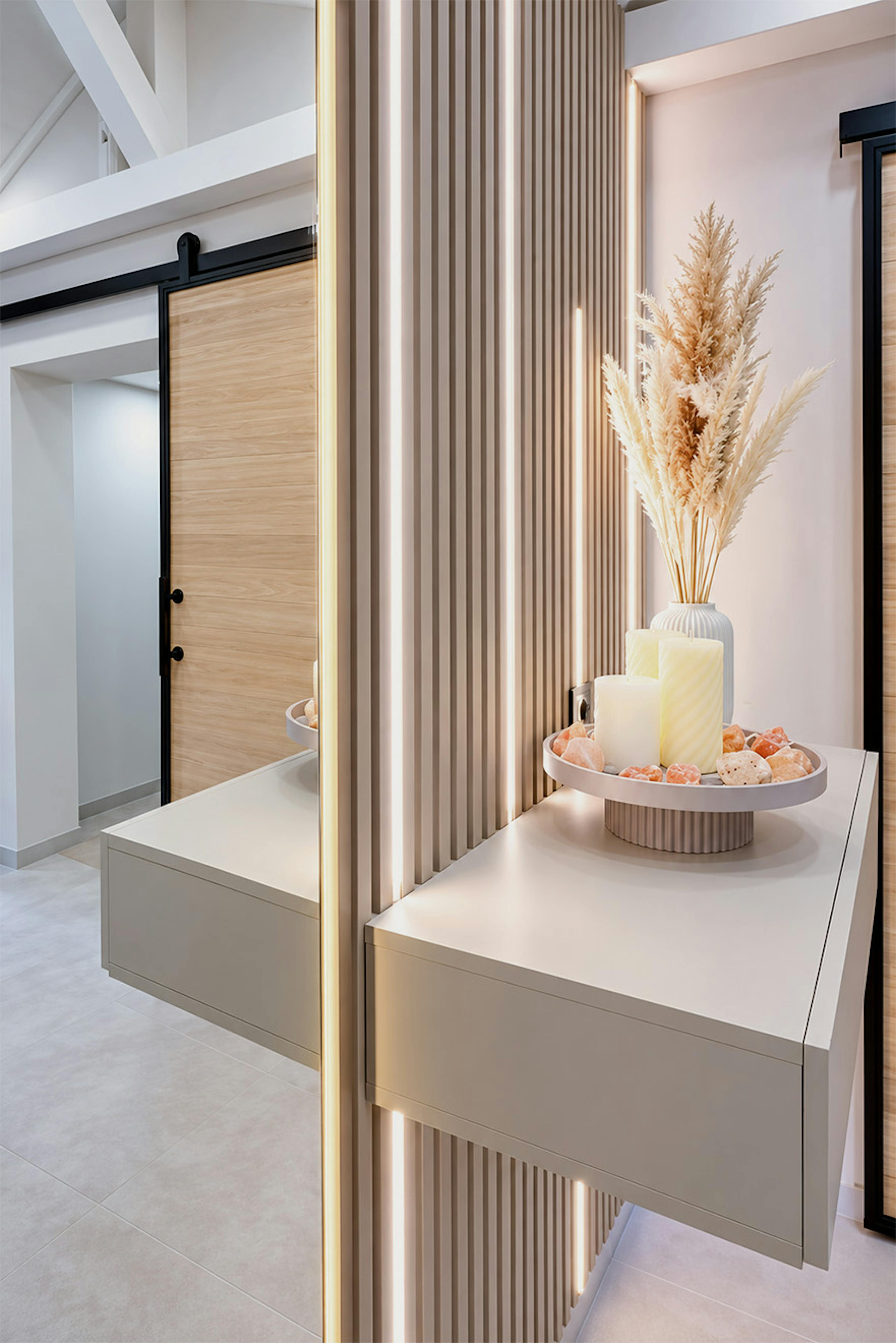 Une console suspendue moderne, sur laquelle sont disposées des bougies décoratives sur un plateau, fixée à un mur à lattes équipé d'un éclairage LED.