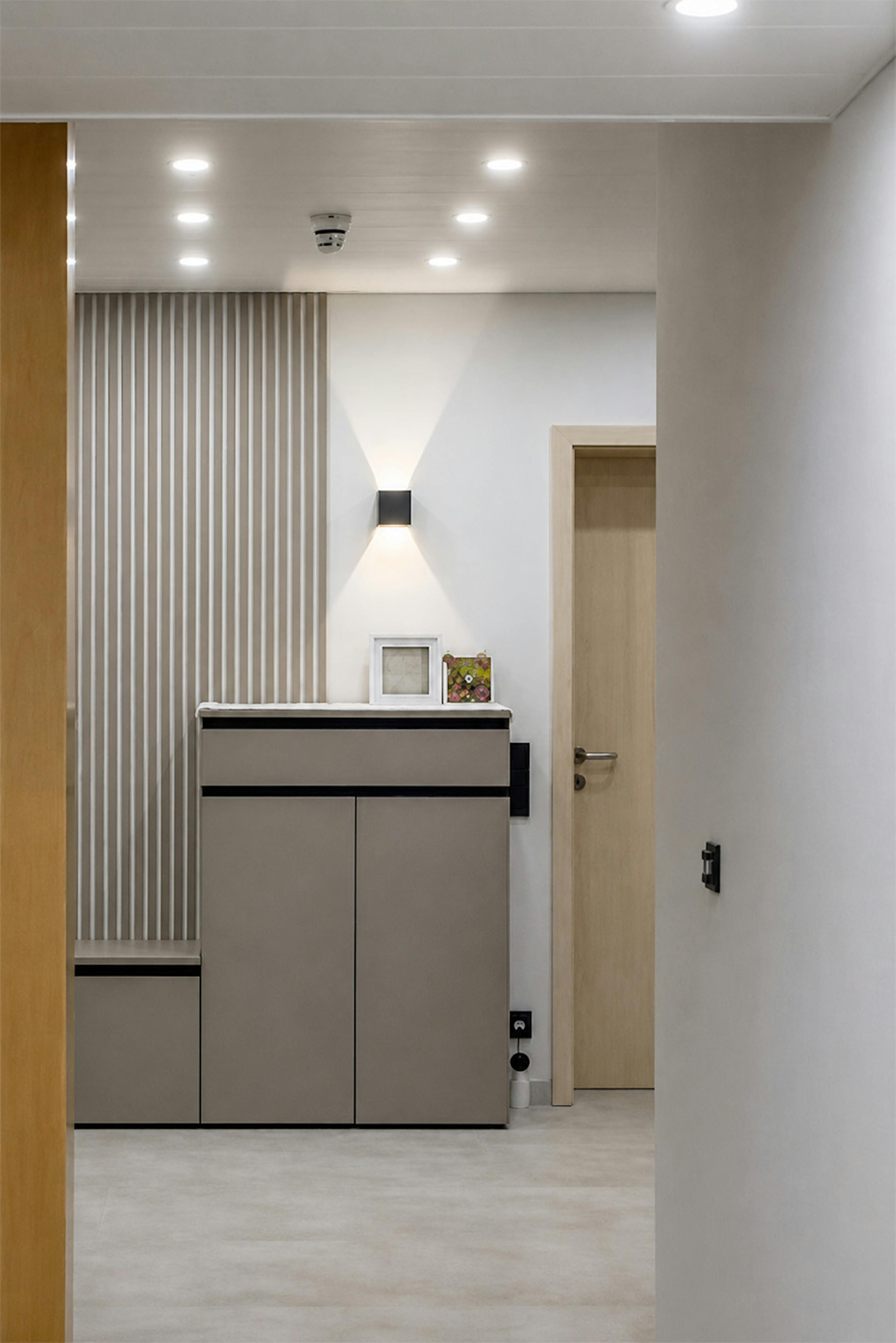 Un couloir doté d'un mobilier encastré minimaliste dans des tons de beige et de gris. Une applique murale moderne est fixée au mur, diffusant une lumière chaude et ciblée.