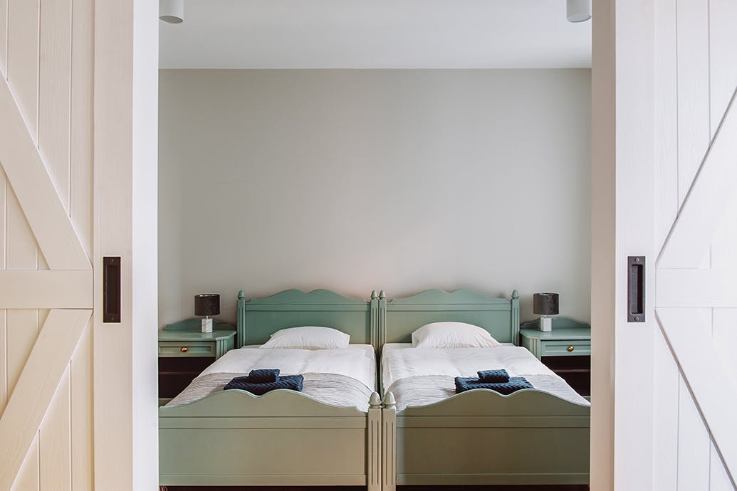 un grand lit couleur sauge derrière une double porte blanche
