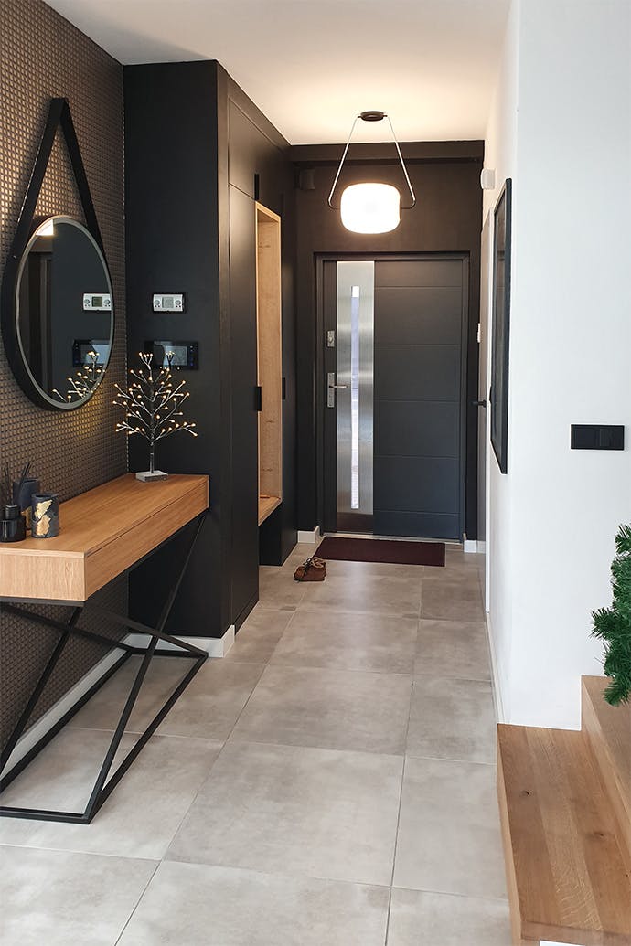 un miroir rond, une console en bois dans le hall aux murs noirs