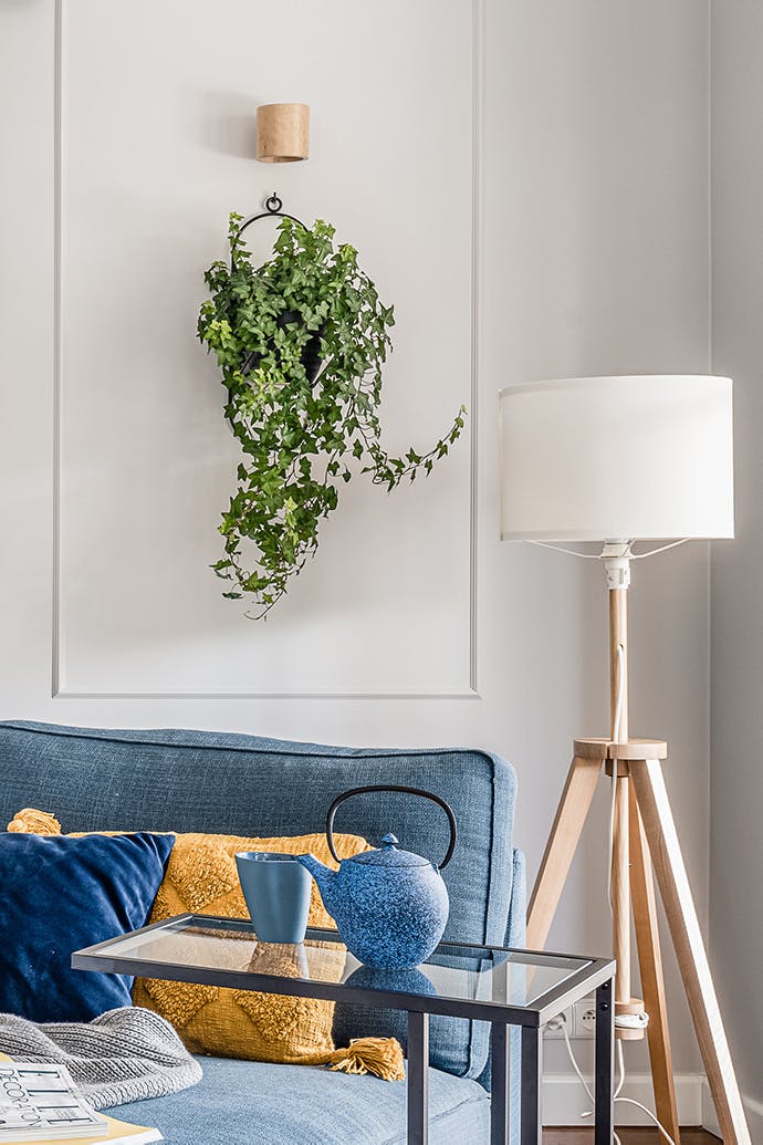 Parterre de fleurs mural en métal noir dans un coin lecture avec un canapé bleu et un lampadaire en bois