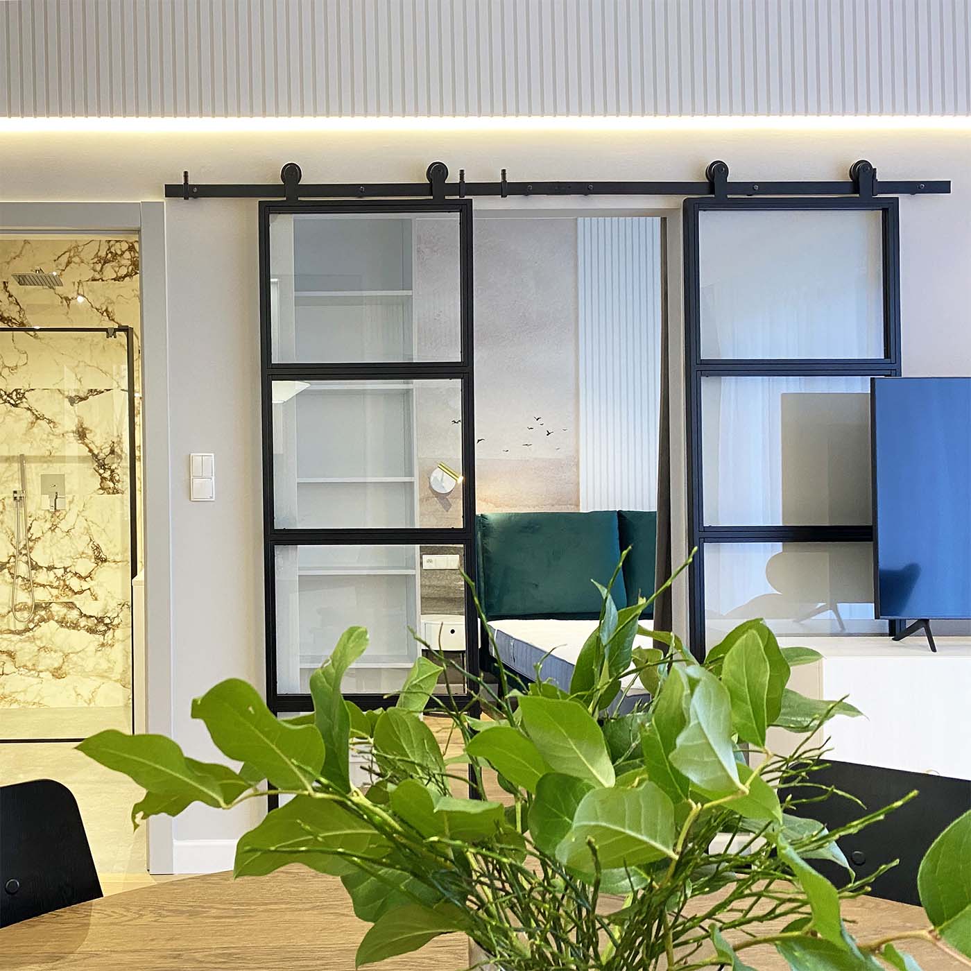 Doppelschiebetüren aus Metall mit Glas, die das Wohnzimmer vom Schlafzimmer in einer modernen Wohnung trennen