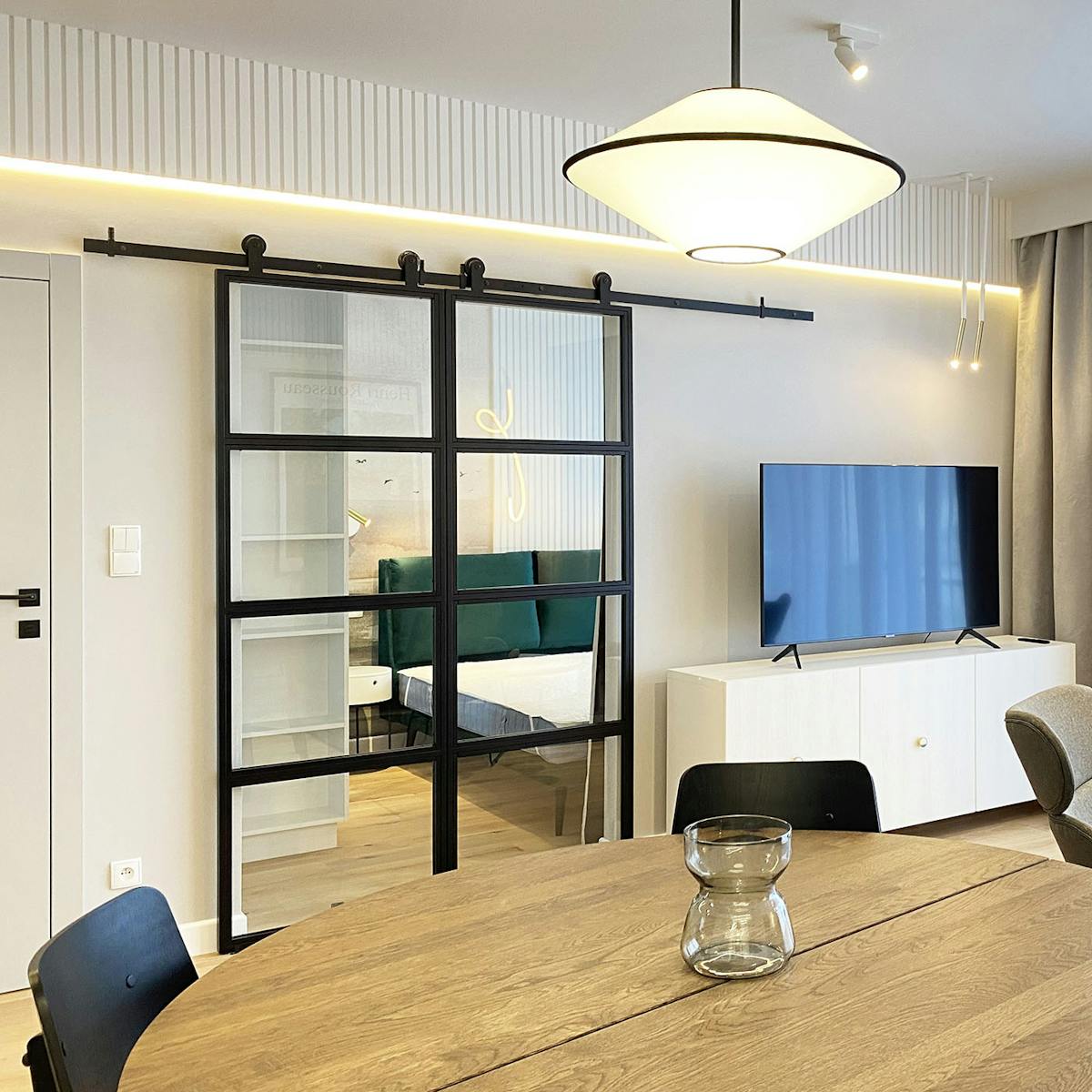 podwójne, szklane drzwi przesuwne w metalowej ramie oddzielające salon od sypialni w nowoczesnym mieszkaniu