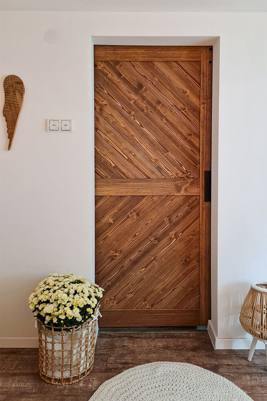 Holzschiebetüren, die den Eingang zum Schlafzimmer in einem skandinavischen Interieur schließen, Blumendekorationen in einem Weidenkorb, weiße Wände im Inneren