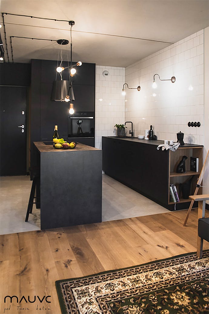 Une cuisine ouverte en noir et blanc, éclairée par des lampes en métal au style industriel