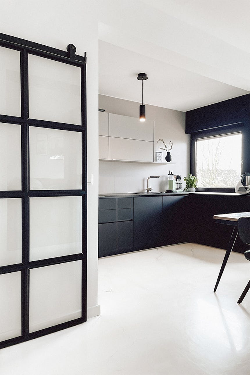 schwarz-weiße Küche, offene Küche mit Essbereich, minimalistische Küche mit schwarz-weißen Möbeln, heller Boden in der Küche, Glastür in einem Metallrahmen, minimalistische Pendelleuchte in der Küche