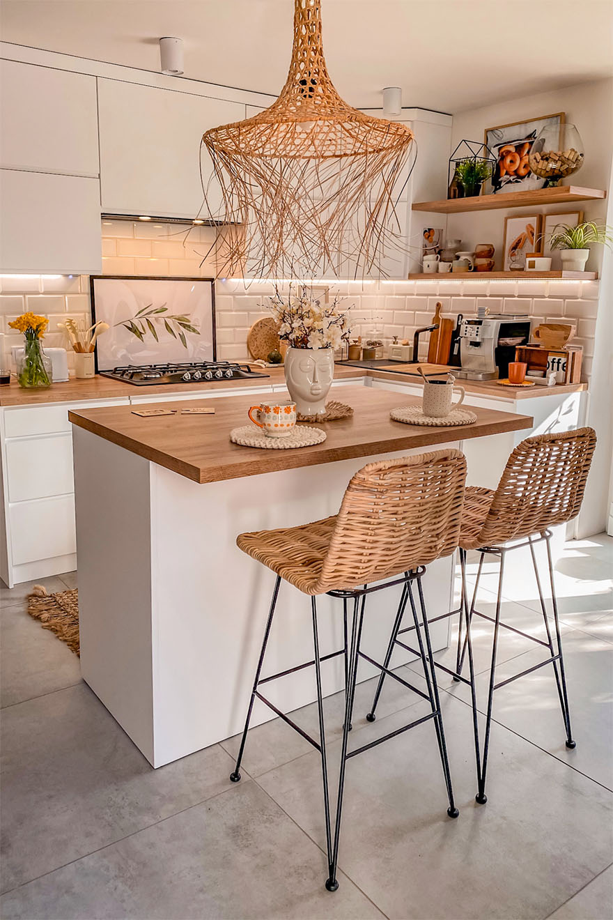 weiße Küche im skandinavischen Stil, Kücheninsel, weiße Küchenmöbel, offene Küche, Holzarbeitsplatten in der Küche, Barhocker aus Korbgeflecht, Hängelampe mit Lampenschirm aus durchbrochenem Bast