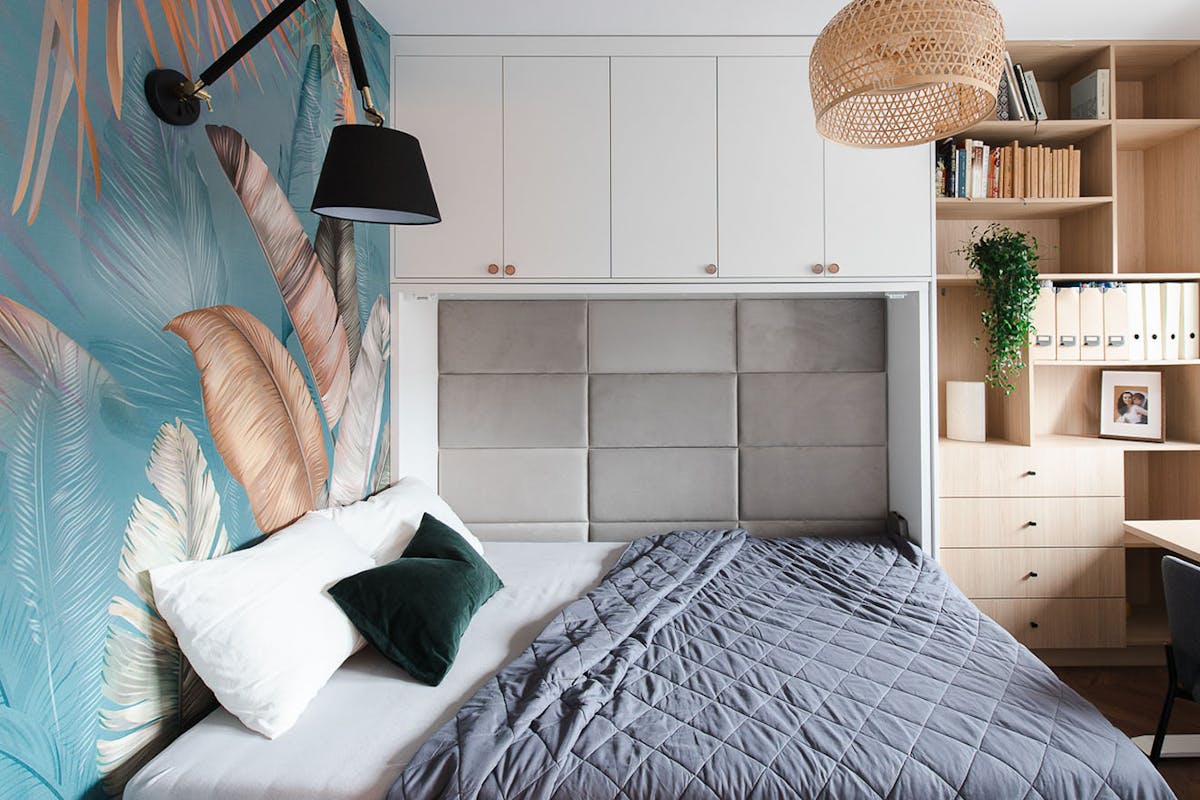 ein im Kleiderschrank verstecktes Bett und bunte Tapeten an der Wand in einem kleinen Schlafzimmer