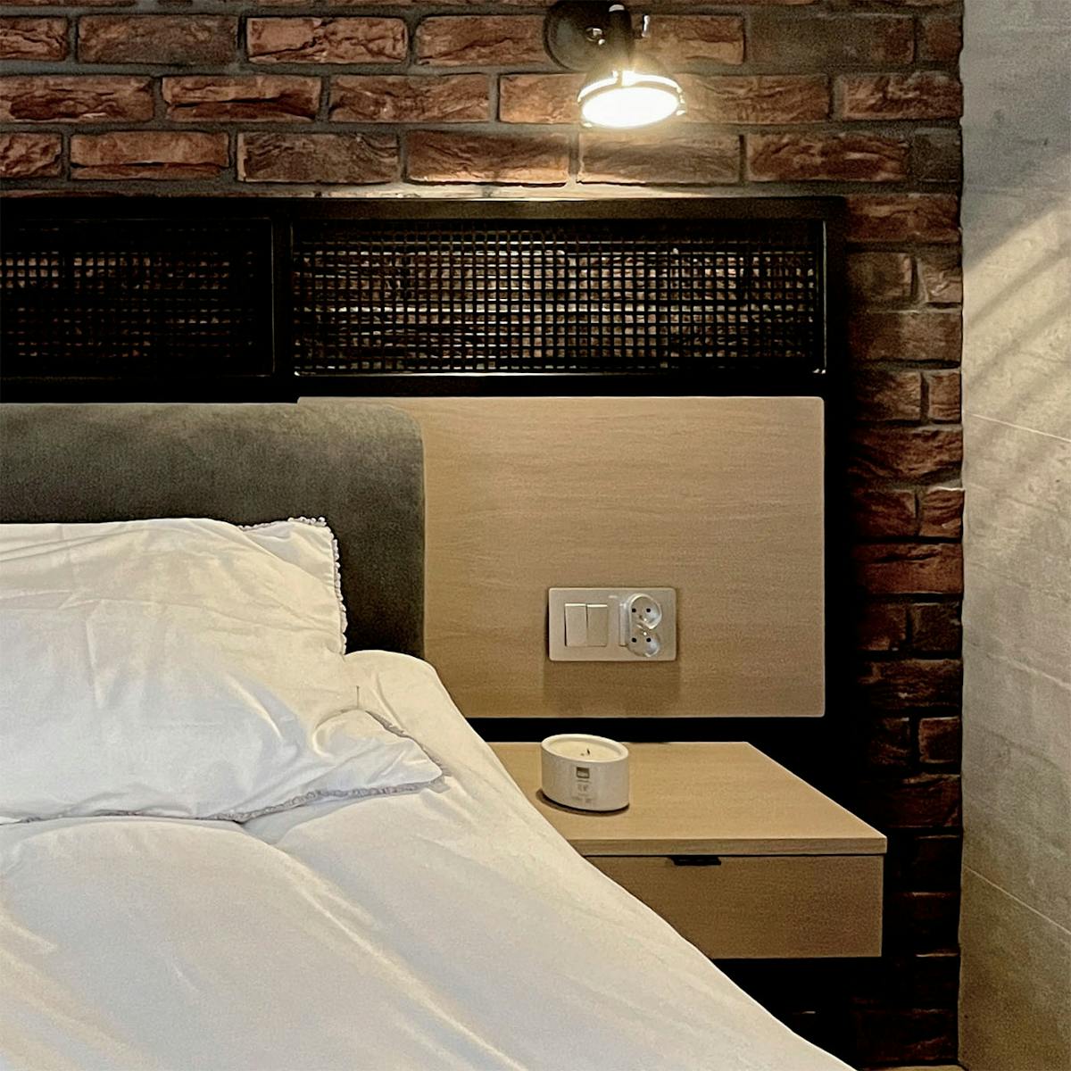 roter Backstein an der Wand in einem industriellen Schlafzimmer, Loft-Nachttisch, dekorative Metallplatte hinter dem Bett in einem industriellen Schlafzimmer