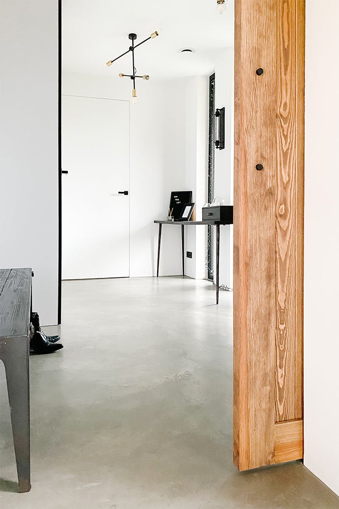 Une porte entrouverte du vestibule décorée en blanc et noir avec un sol en ciment