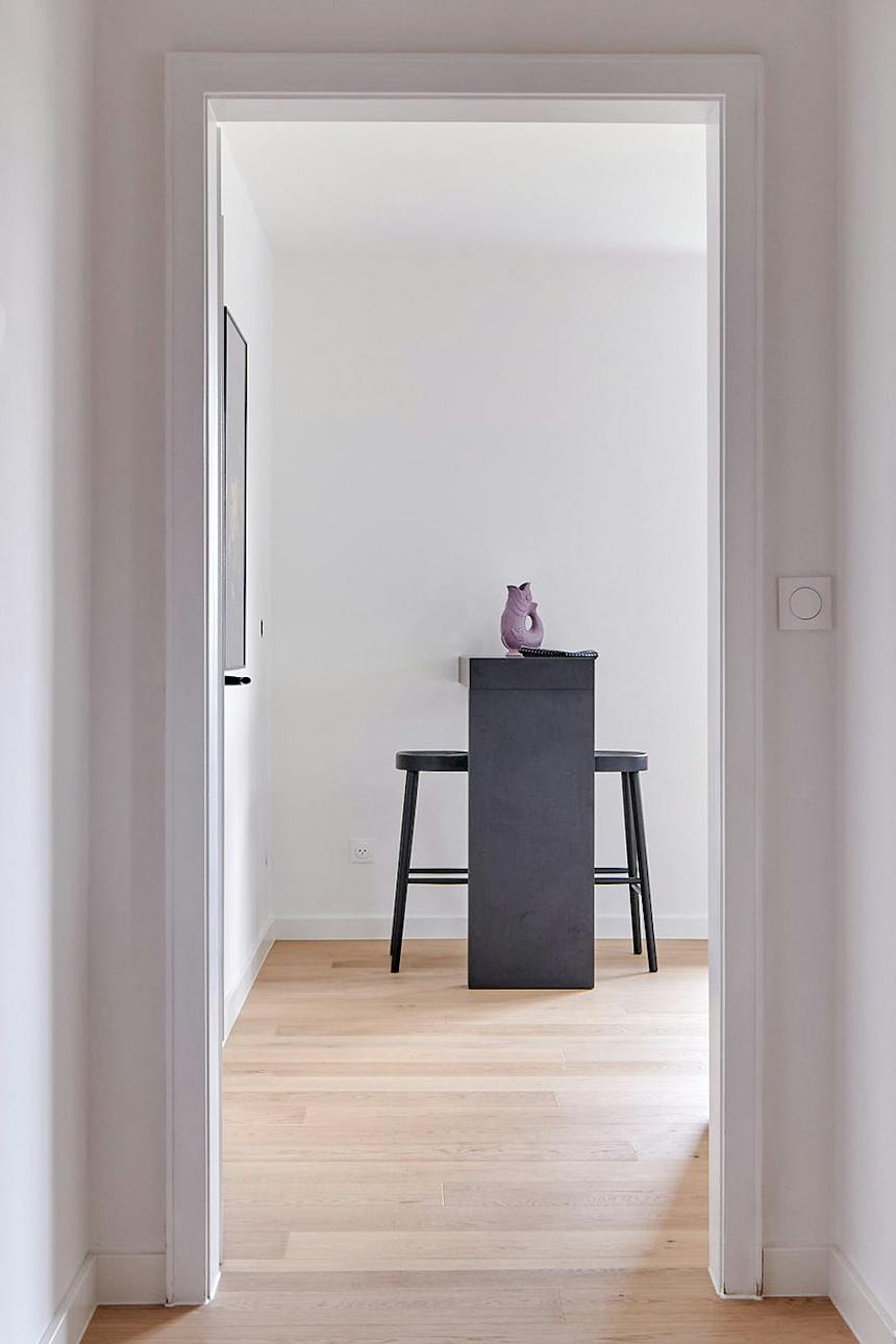Blick durch den Türrahmen auf einen höheren Tisch mit schwarzen Barhockern in einem modernen, hellen Raum.