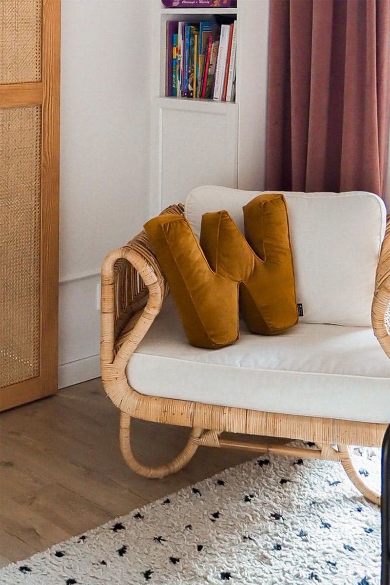 un oreiller à lettres et un fauteuil en osier dans la chambre d'une fille