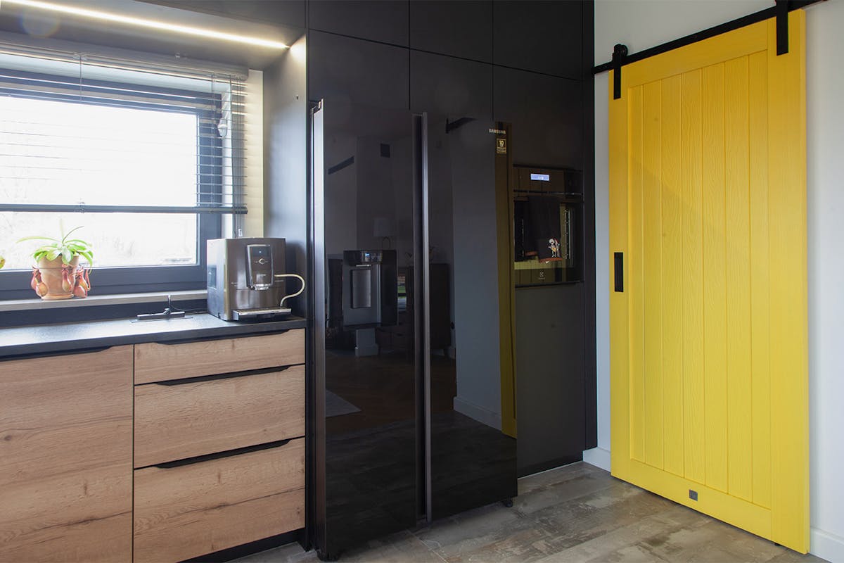 gelbe Speisekammer-Schiebetür in der Küche mit schwarzen Schränken