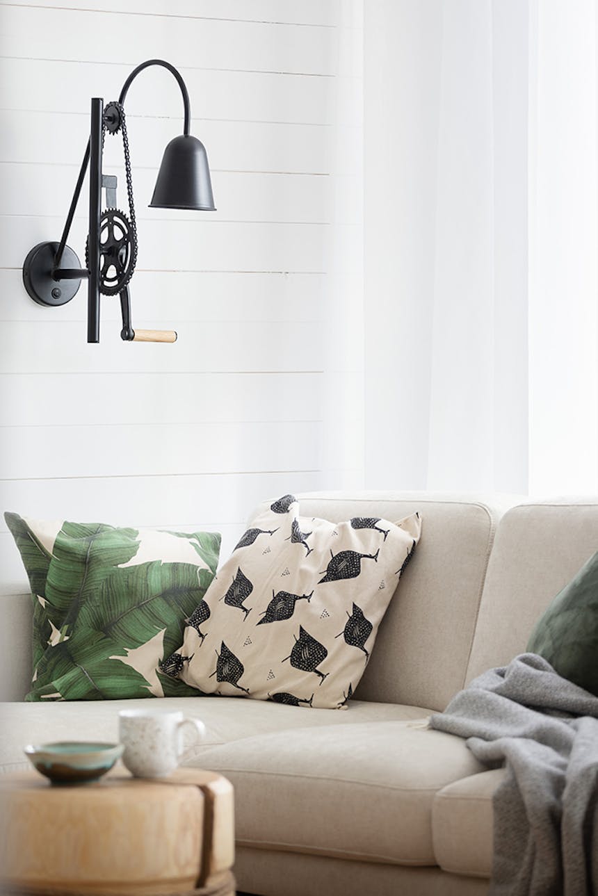 schwarze Industrielampe an weißer Wand, hellbraunes Sofa, dekorative Kissen