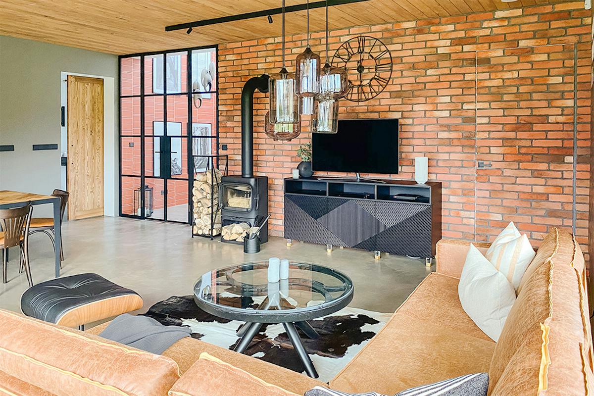Wohnzimmer im Industrie loft stil, Mikrozement Boden, Holzdecke, schwarze Metallelemente, schwarzer Kamin im Wohnzimmer, Glas- und Stahllampe, Couchtisch aus Glas, Backsteinmauer im Wohnzimmer