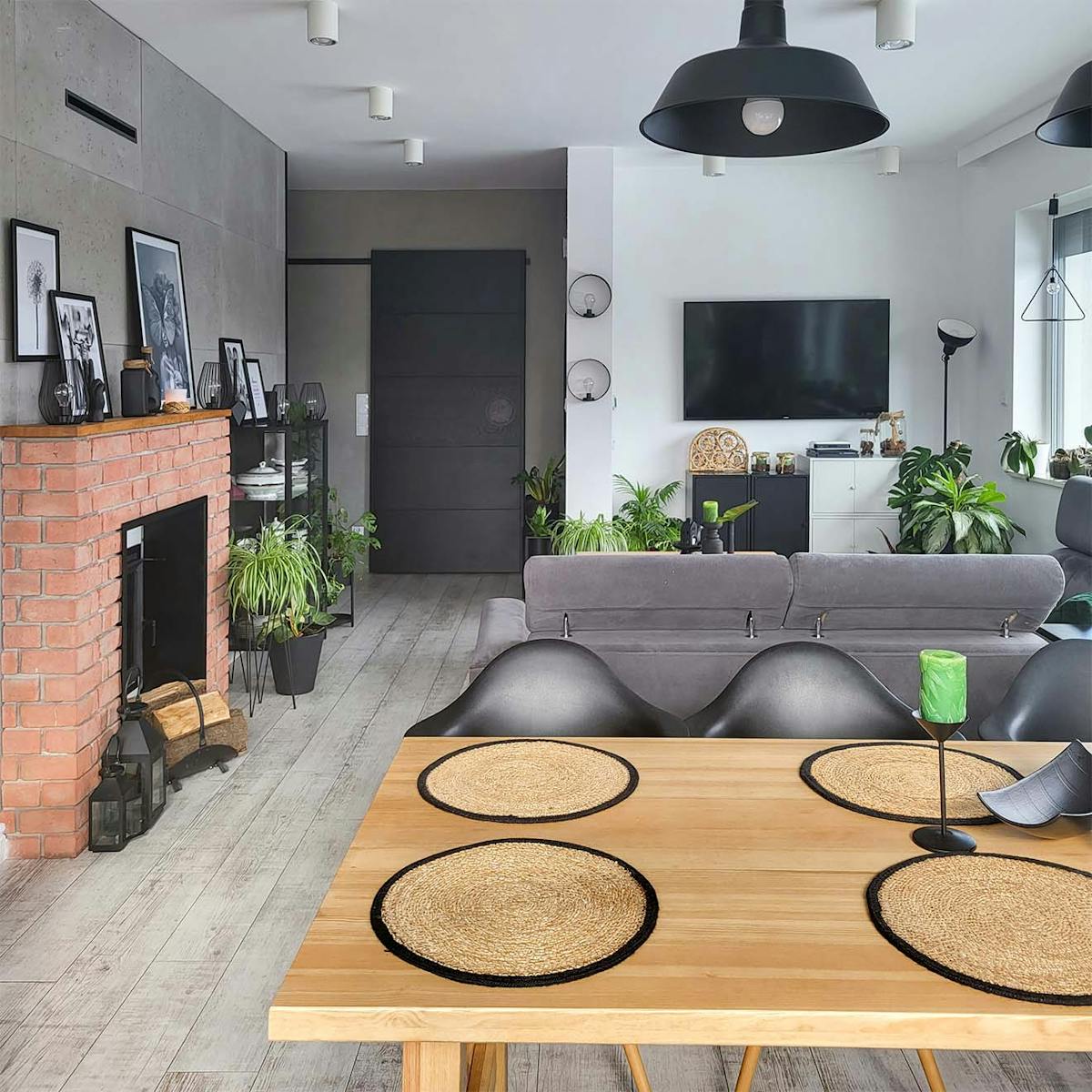 Esstisch aus Holz, Kamin aus rotem Backstein und schwarze Schiebetüren in einem in Grautönen gehaltenen Wohnzimmer