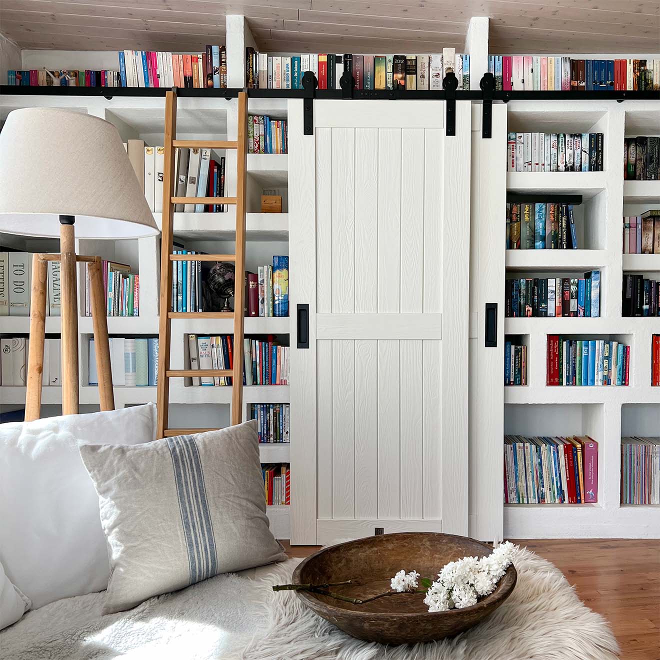 podwójne drzwi białe i drabinka na ścianie z książkami w domowej bibliotece w salonie