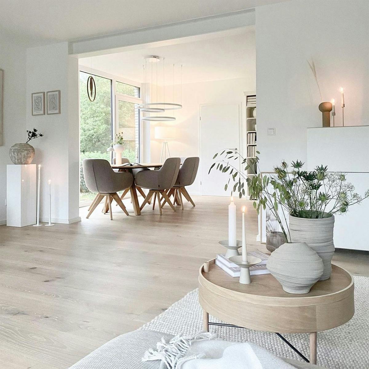 offenes Wohnzimmer, das mit dem Esszimmer verbunden ist, große bequeme Stühle im Esszimmer, runder Tisch im nordischen Stil, Vasen mit Pflanzen, die den Tisch schmücken