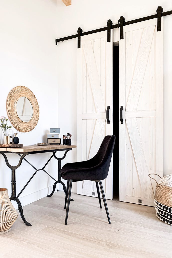des portes coulissantes blanches et étroites fermant l'armoire et une coiffeuse rustique dans la chambre blanche