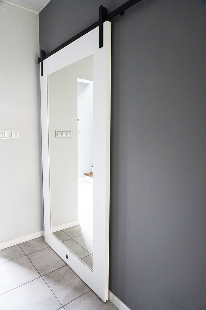 grand miroir coulissant dans un cadre en bois blanc contre un mur gris dans le hall