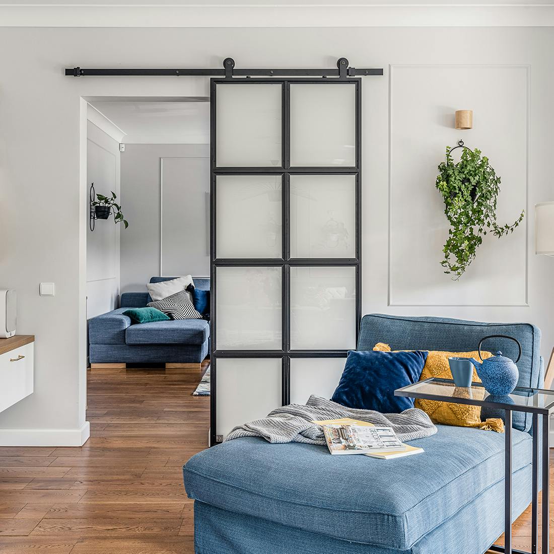 Coin lecture avec un canapé bleu, séparé du salon par une porte coulissante en verre opale