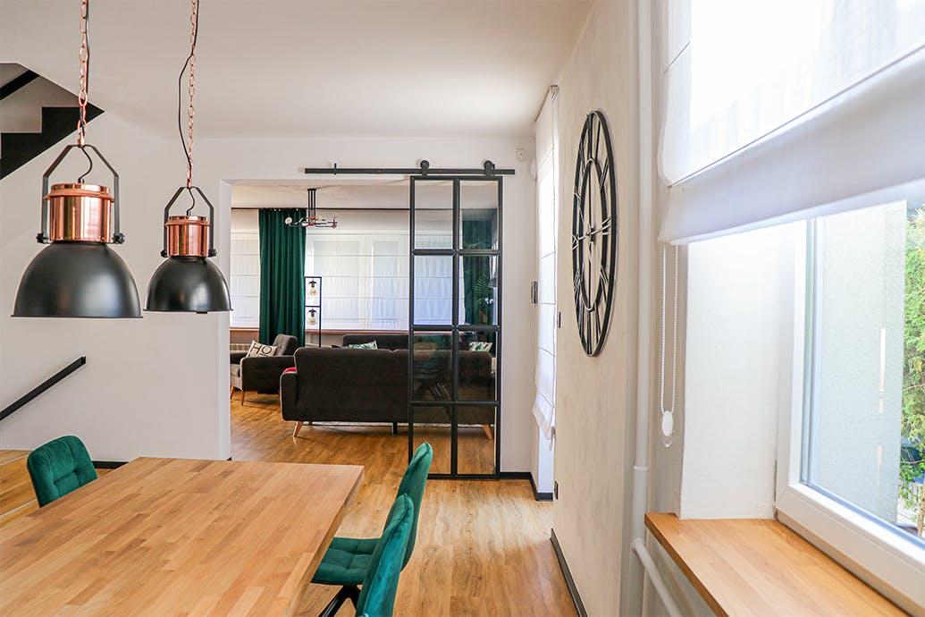 décorations de loft, portes en métal avec verre, portes de loft, portes coulissantes en verre métal, portes en verre dans un cadre noir, chaises de salle à manger vertes, salon ouvert sur la salle à manger, lampes suspendues industrielles dans la salle à manger, grande table à manger en bois