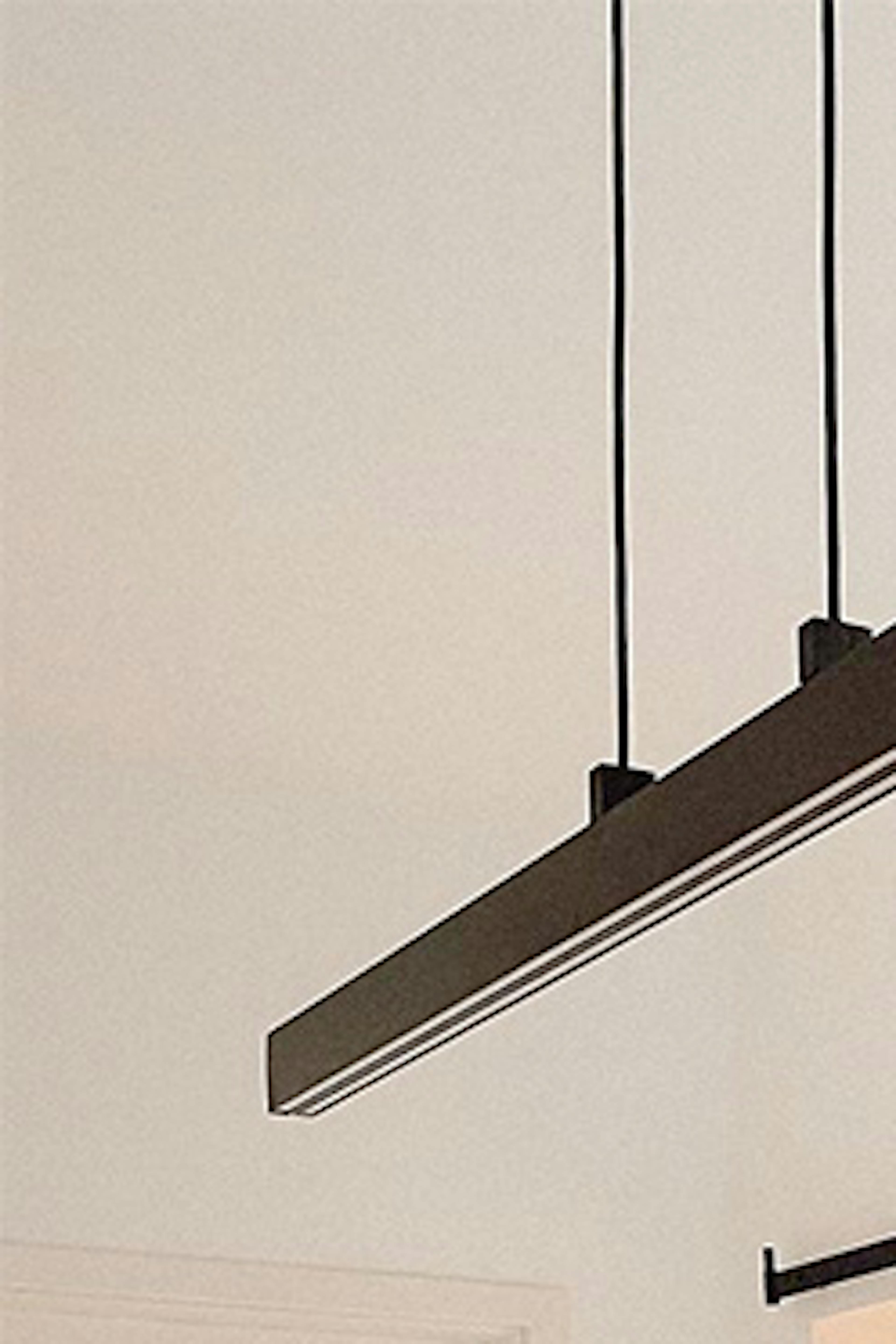Des bougies décoratives, un vase de fleurs séchées sur une table à manger en bois éclairée par une longue lampe minimaliste